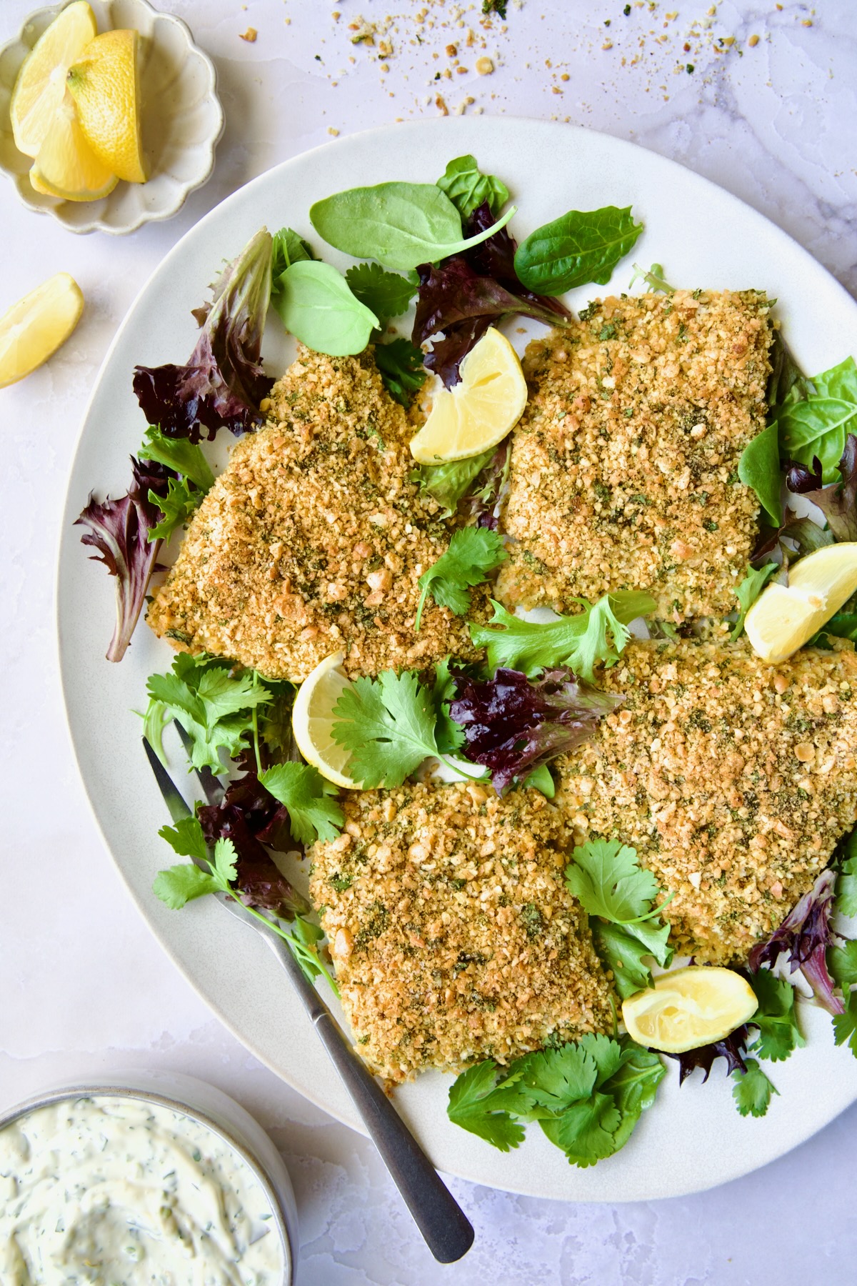 Crispy Chickpea-Crusted Fish on oval white platter garnished with fresh baby greens with serving fork.