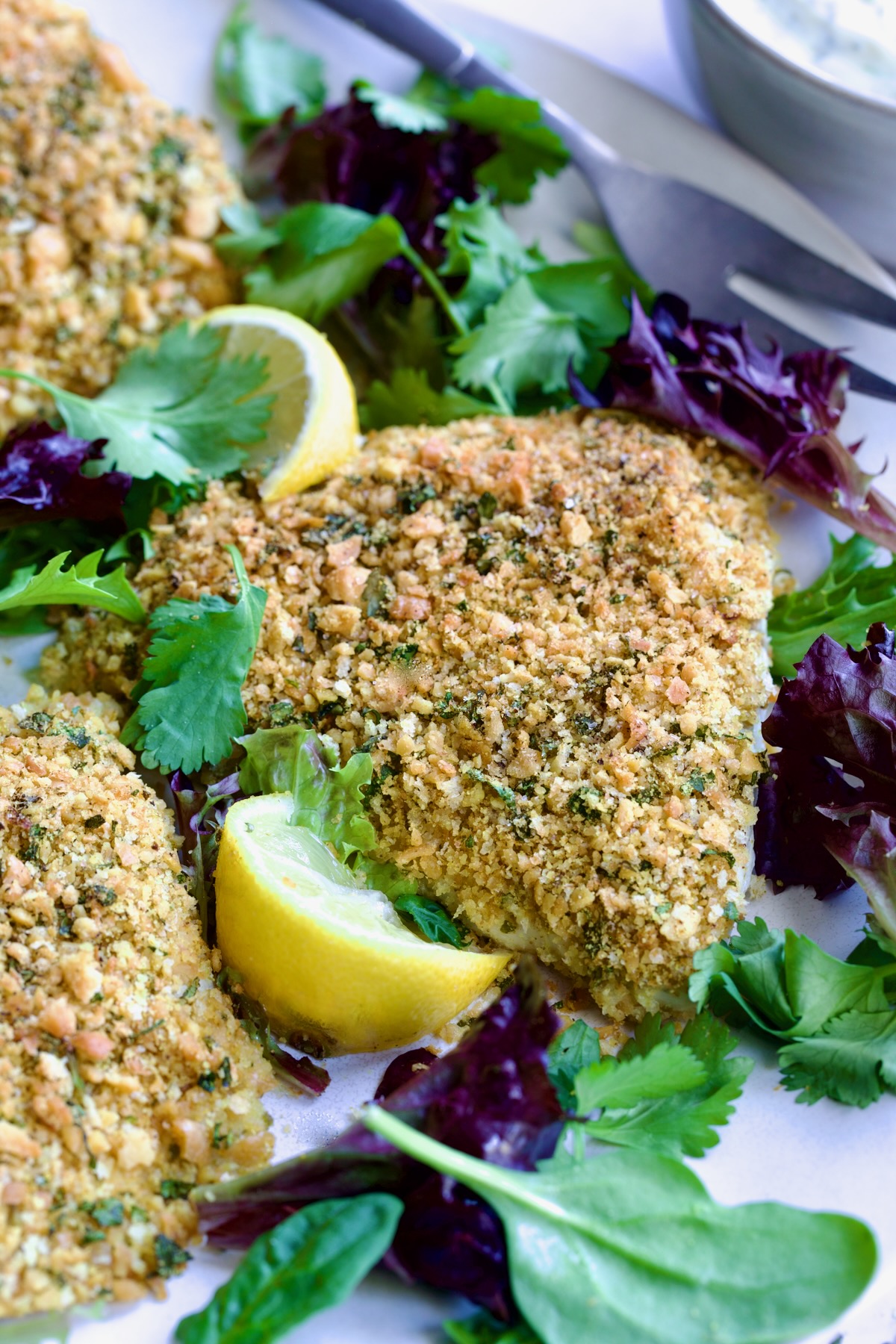 Crispy Chickpea-Crusted Fish on oval white platter garnished with fresh baby greens.