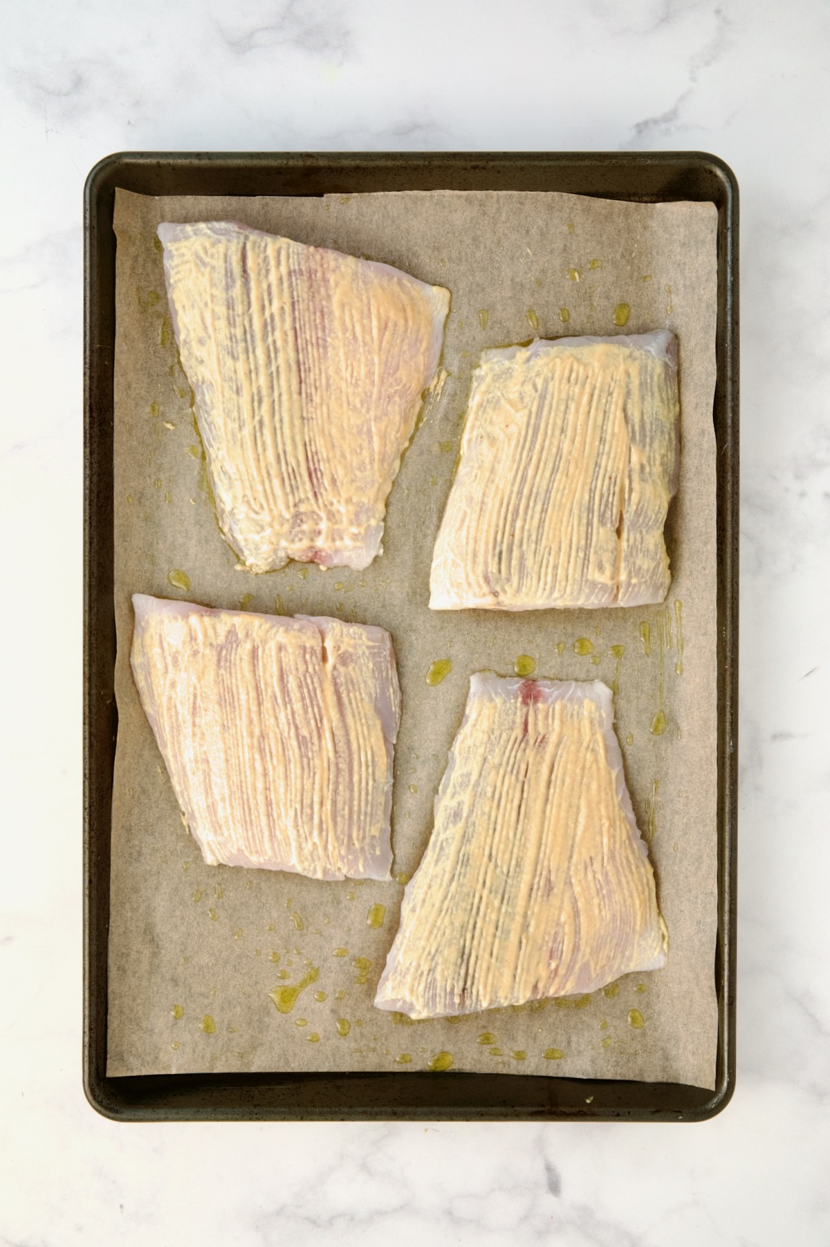 Four pieces of fish on parchment paper-lined baking sheet brushed with mustard before being baked.