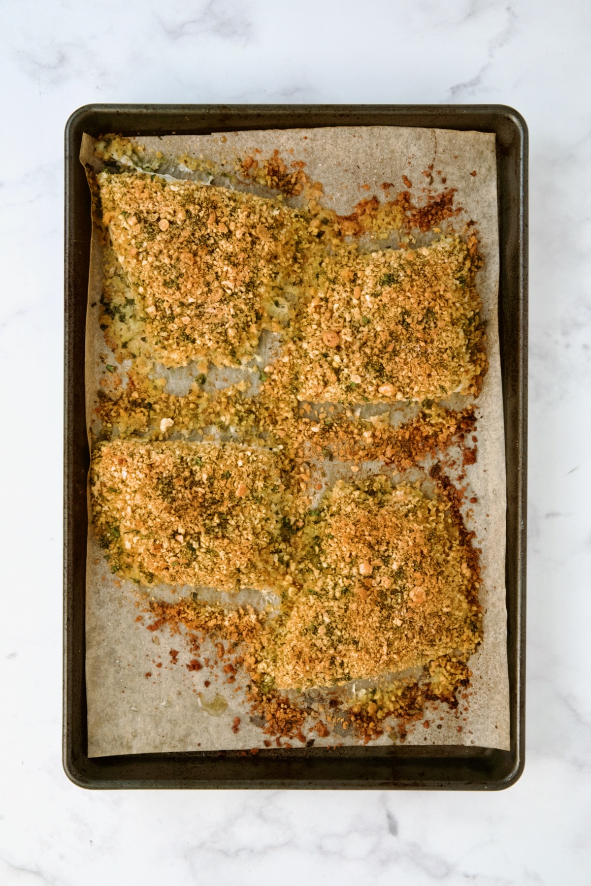 Four pieces of fish on parchment paper-lined baking sheet topped with chickpea topping after being baked.