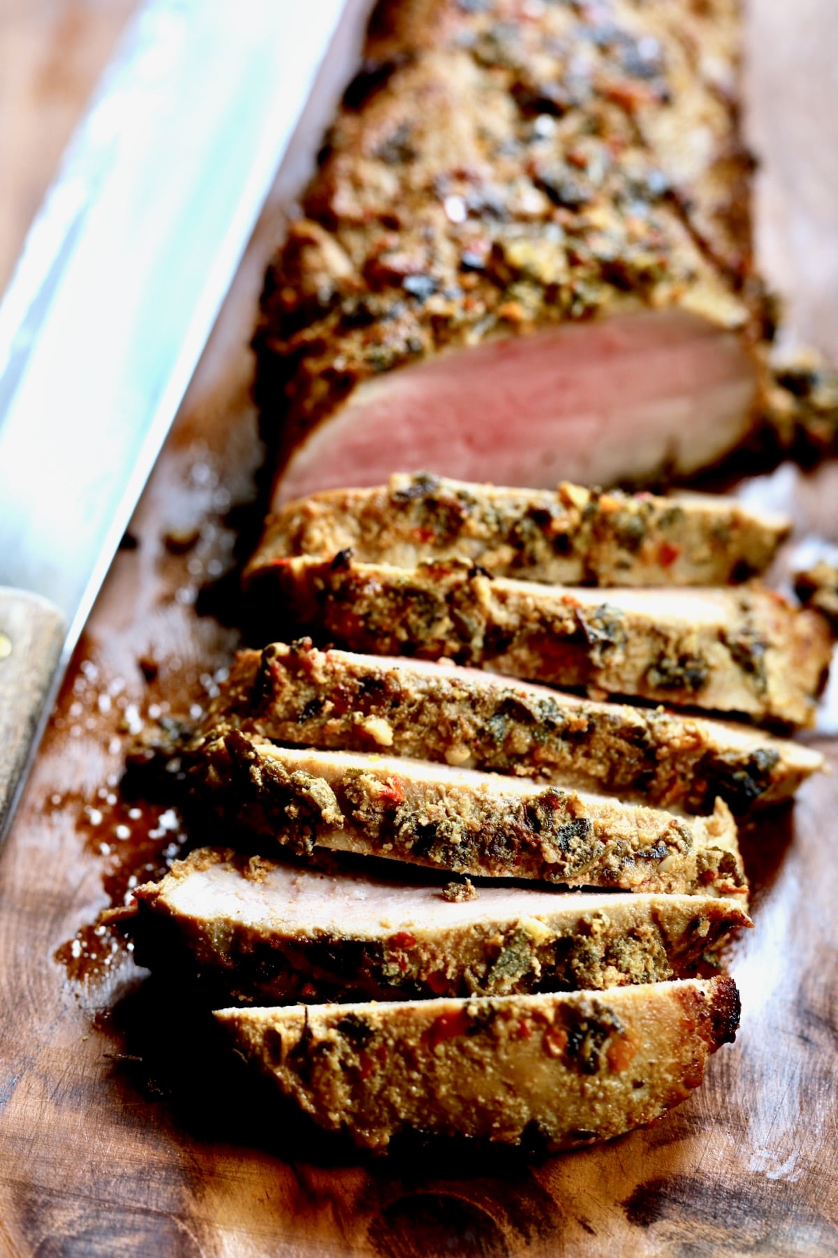 Sliced pork tenderloin on wooden cutting board.
