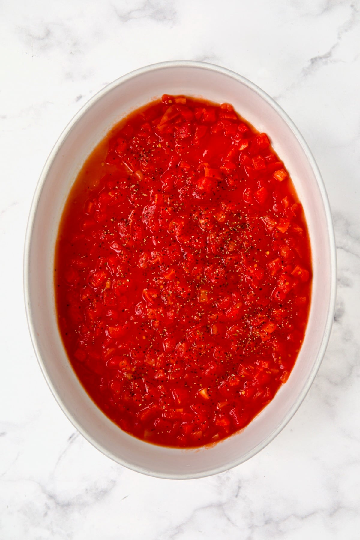 Petite diced tomatoes spread over the bottom of an oval white baking dish.