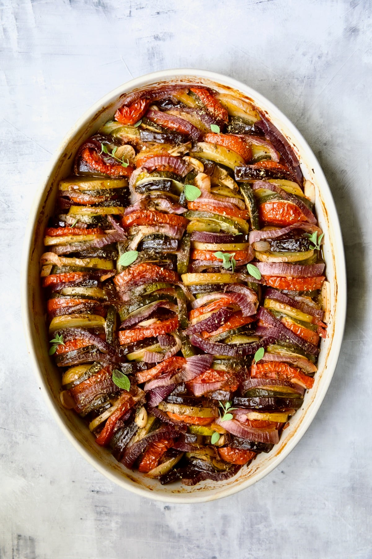 Briam (Greek Roast Vegetables) in oval white gratin dish with serving spoon.