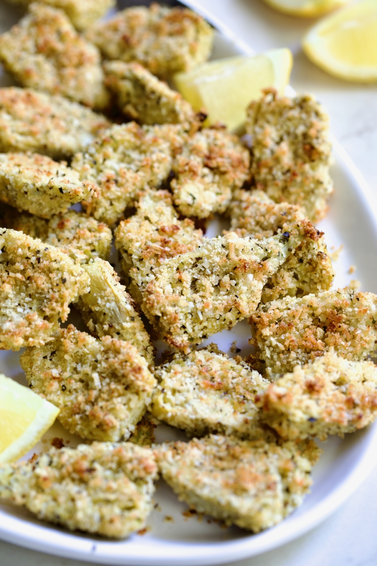 Crispy Parmesan Artichoke Hearts on oval white platter with lemon wedges.