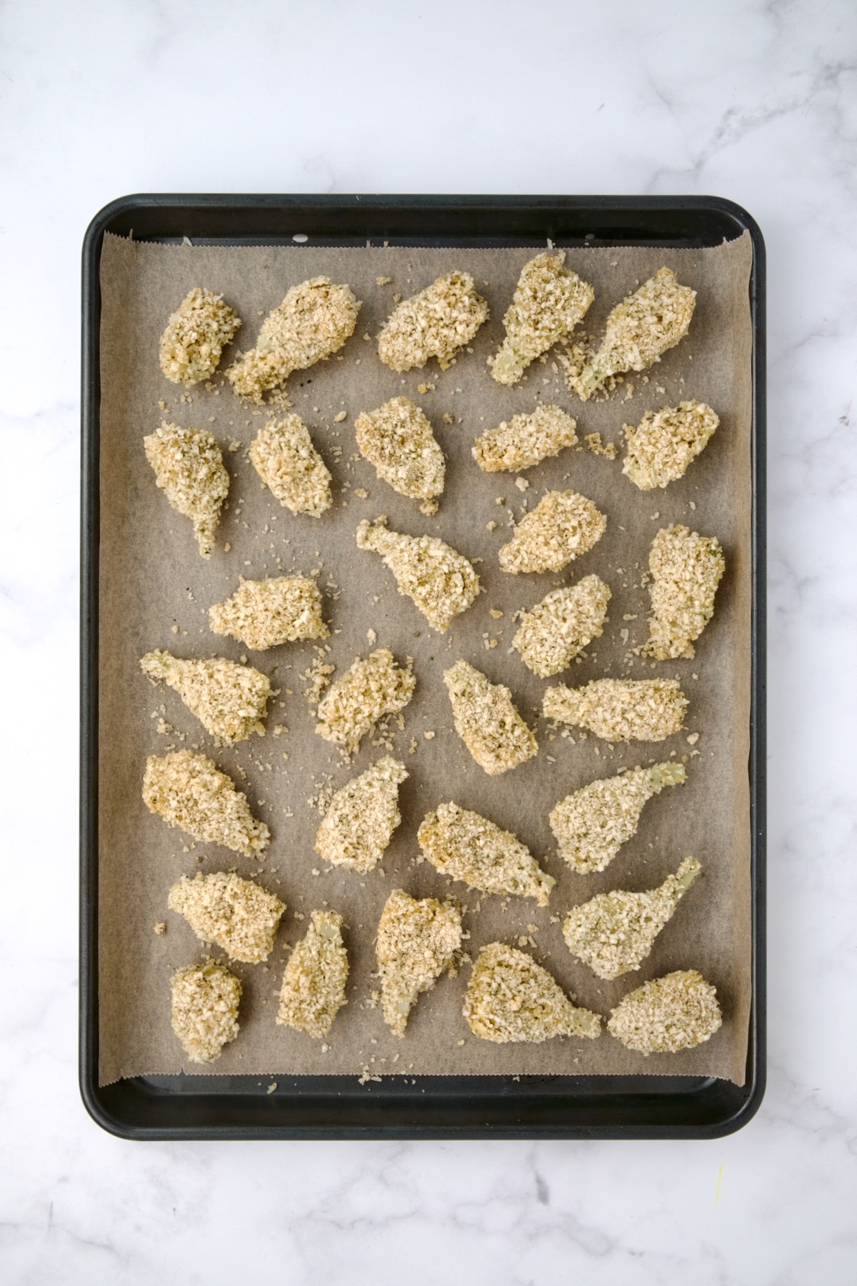 Breaded artichoke hearts on parchment paper-lined baking sheet before being baked.