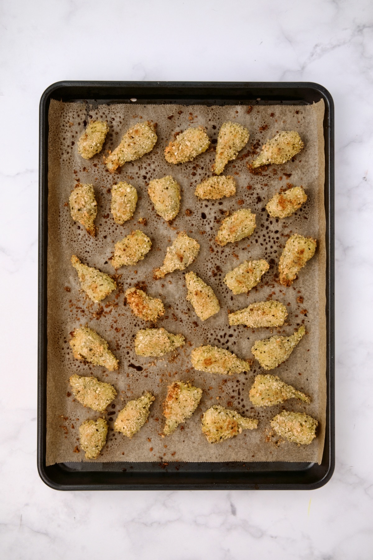 Breaded artichoke hearts on parchment paper-lined baking sheet after being baked.
