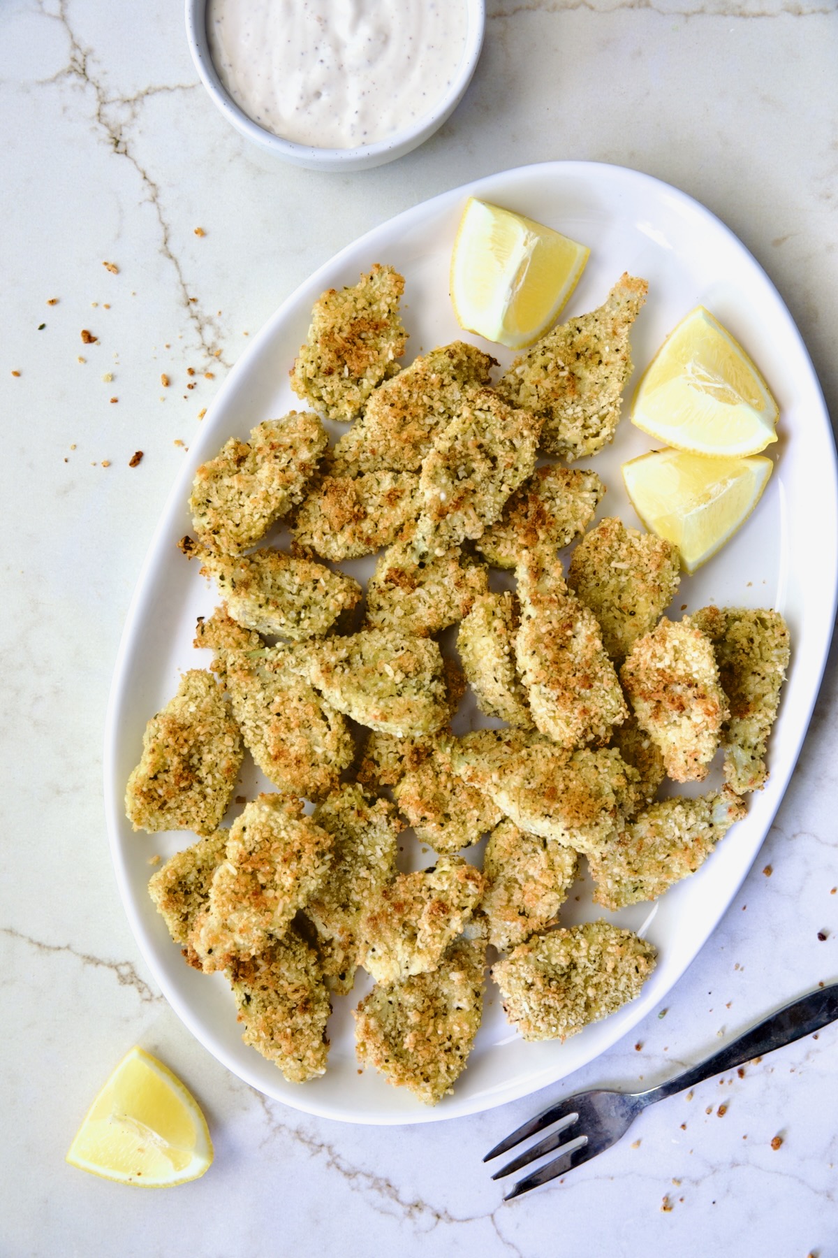 Crispy Parmesan Artichoke Hearts on oval white platter with lemon wedges.