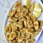 Crispy Parmesan Artichoke Hearts on oval white platter with lemon wedges.