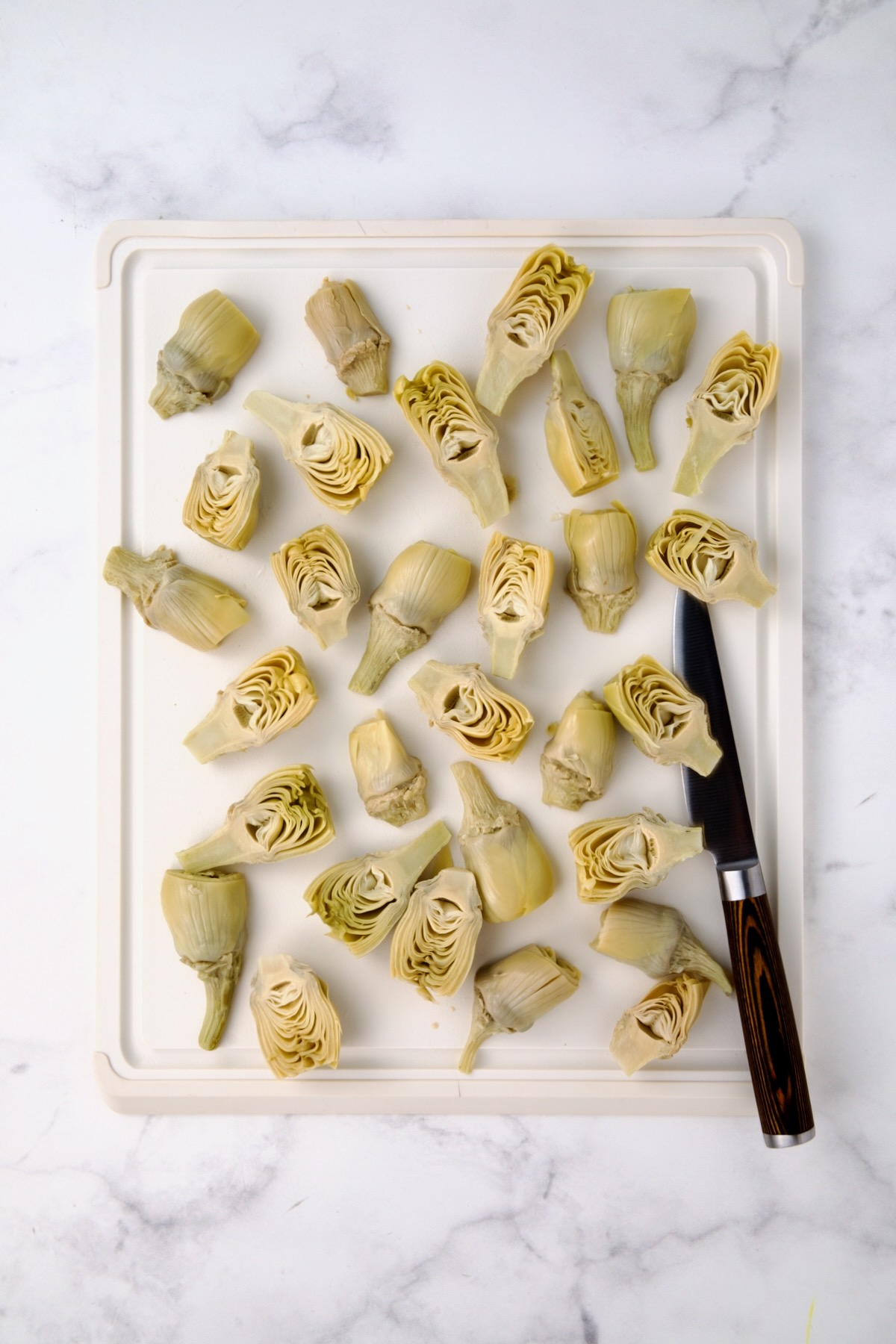 Halved artichoke hearts on white plastic cutting board.