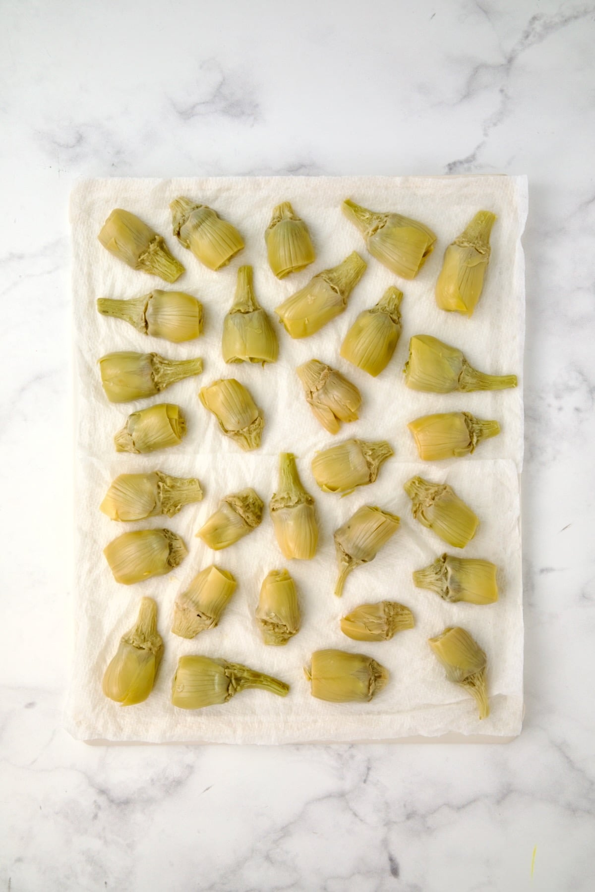 Halved artichoke hearts being drained on paper towels.