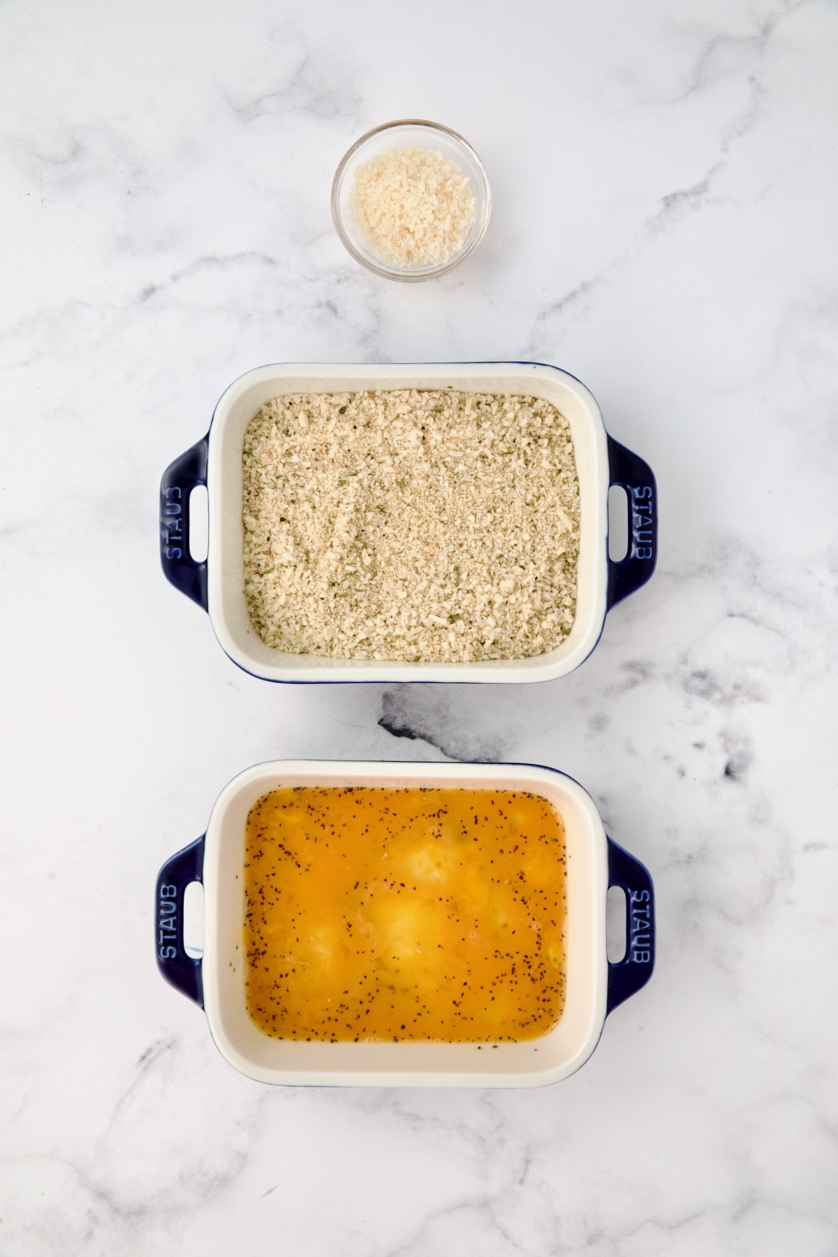 Three containers with parmesan cheese in one, breadcrumbs in another and eggs in a third.