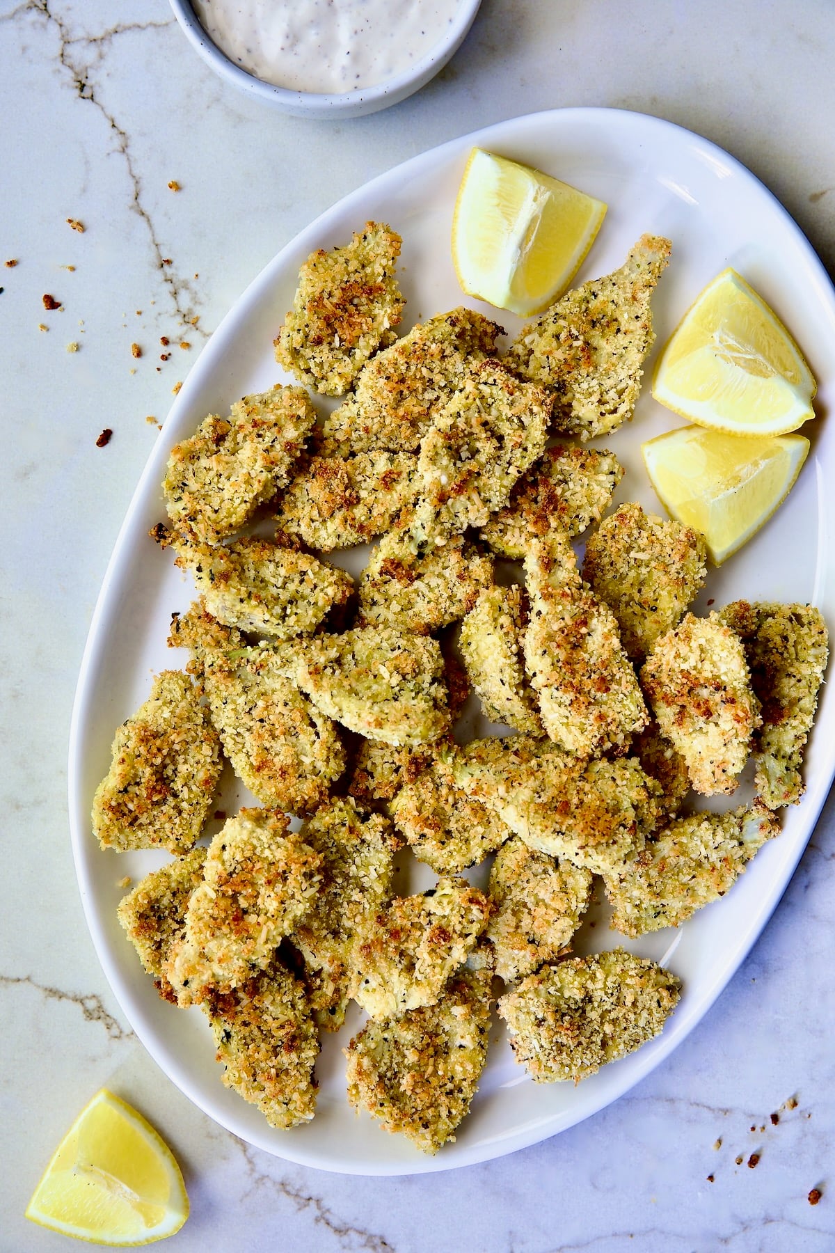 Crispy Parmesan Artichoke Hearts on oval white platter with lemon wedges.
