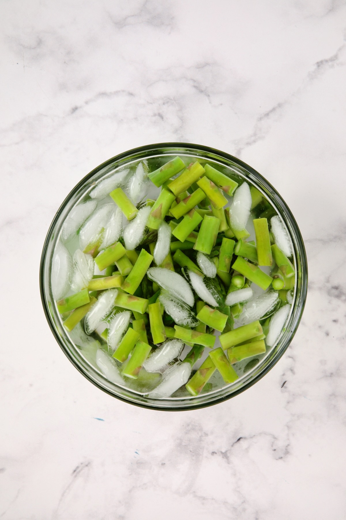 Asparagus pieces in ice bath in glass bowl.