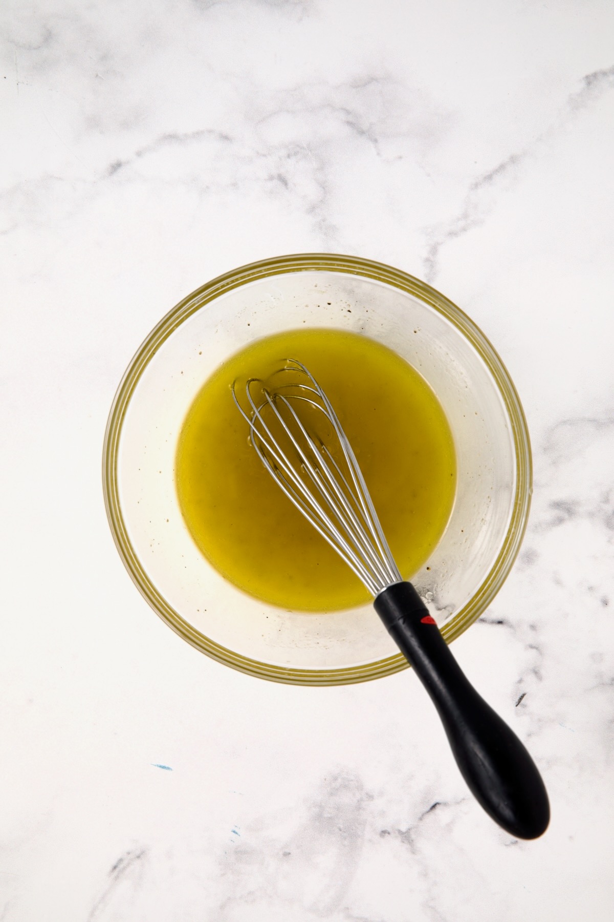 Lemon vinaigrette in glass bowl with black-handled whisk.