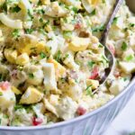Potato Salad with Horseradish Dressing in light blue bowl with serving spoon garnished with parsley.