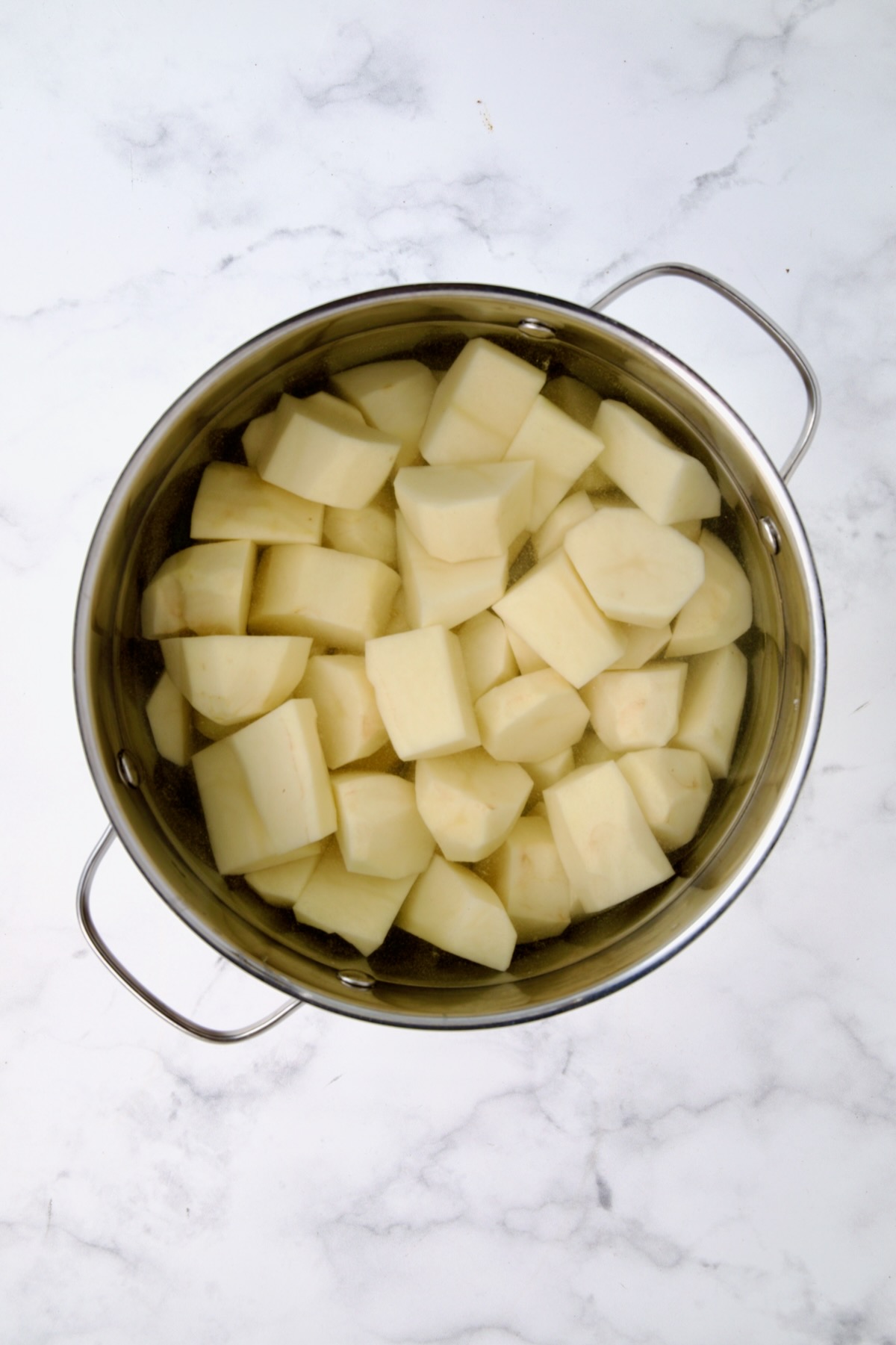 Uncooked peeled potatoes in water in stainless steel pot.