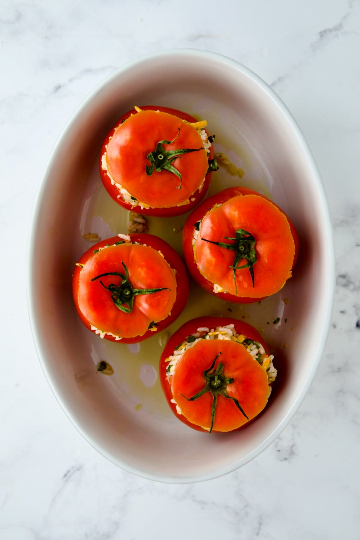 Four round cheese and rice-stuffed tomatoes in oval baking dish before being baked with the tomato tops placed back on top.