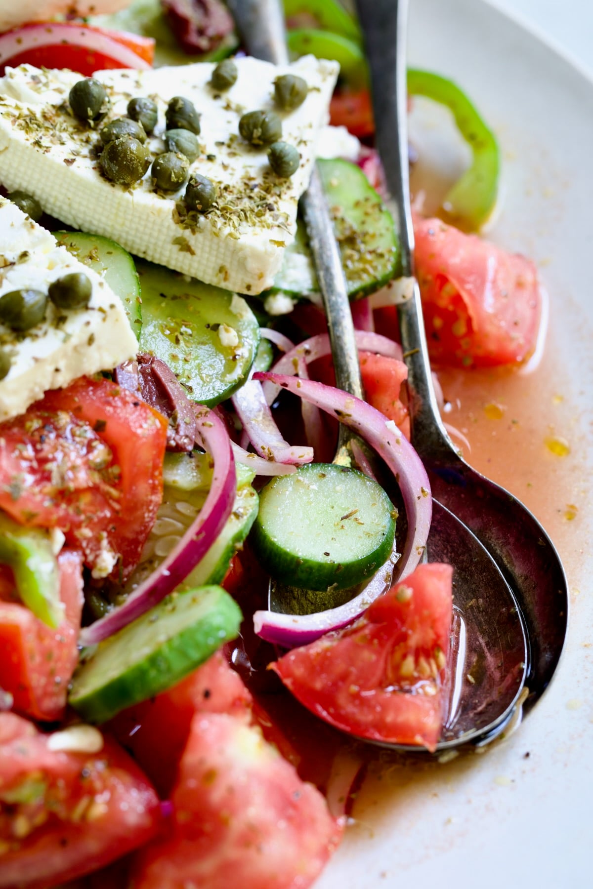 Close-up of Classic Greek Salad on white oval platter with serving utensils.