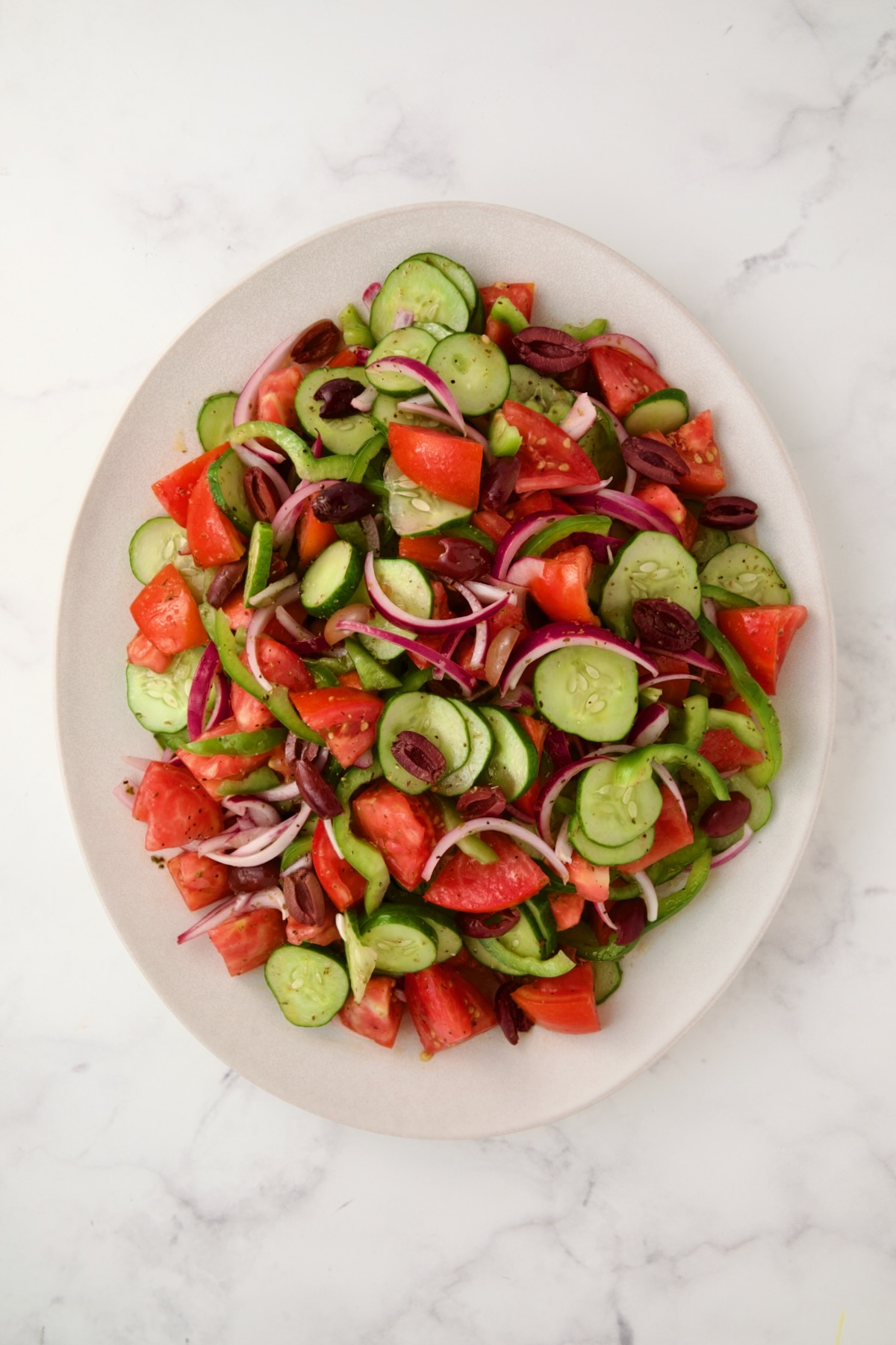 Greek salad on white oval platter before cheese is added.