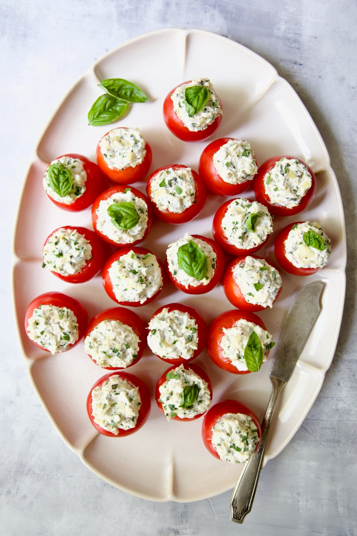 Cream Cheese and Artichoke Stuffed Tomatoes on oval white platter garnished with fresh basil leaves.