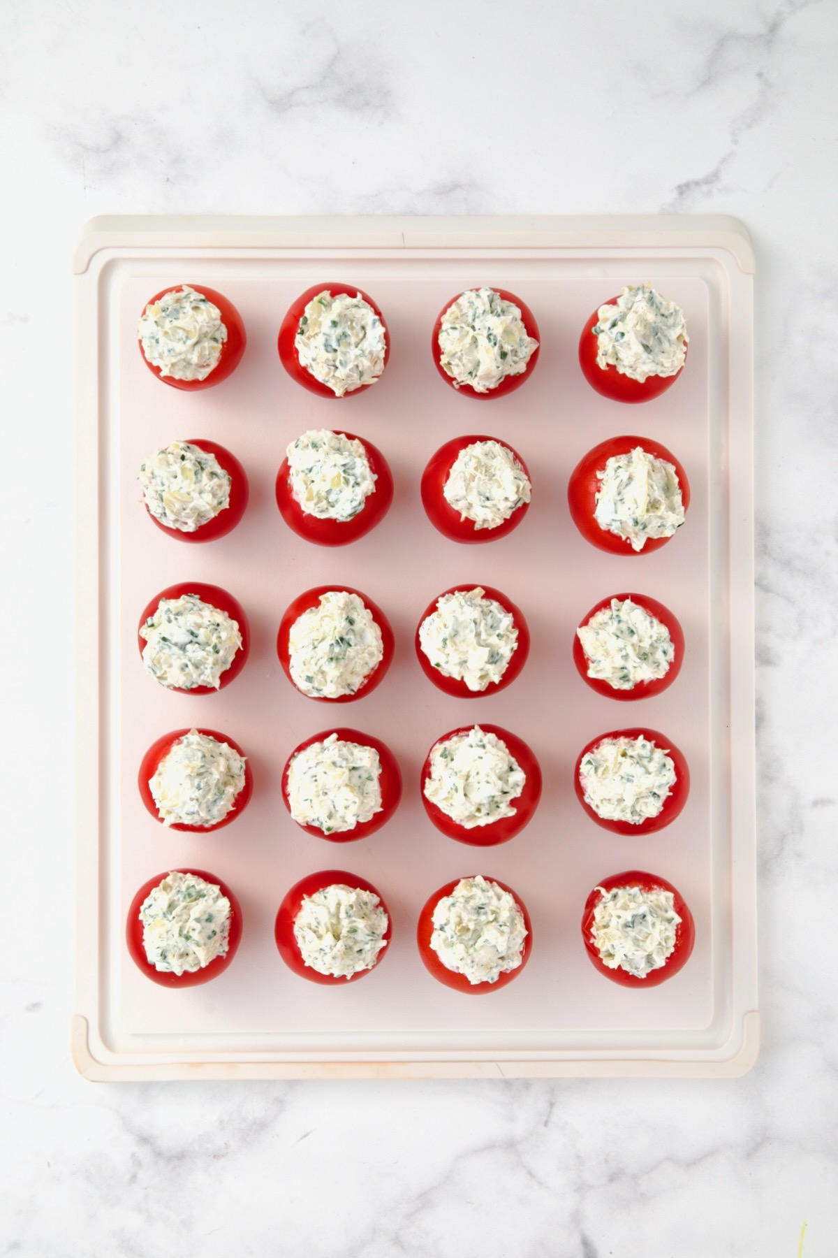 20 stuffed Campari tomatoes on white plastic cutting board.