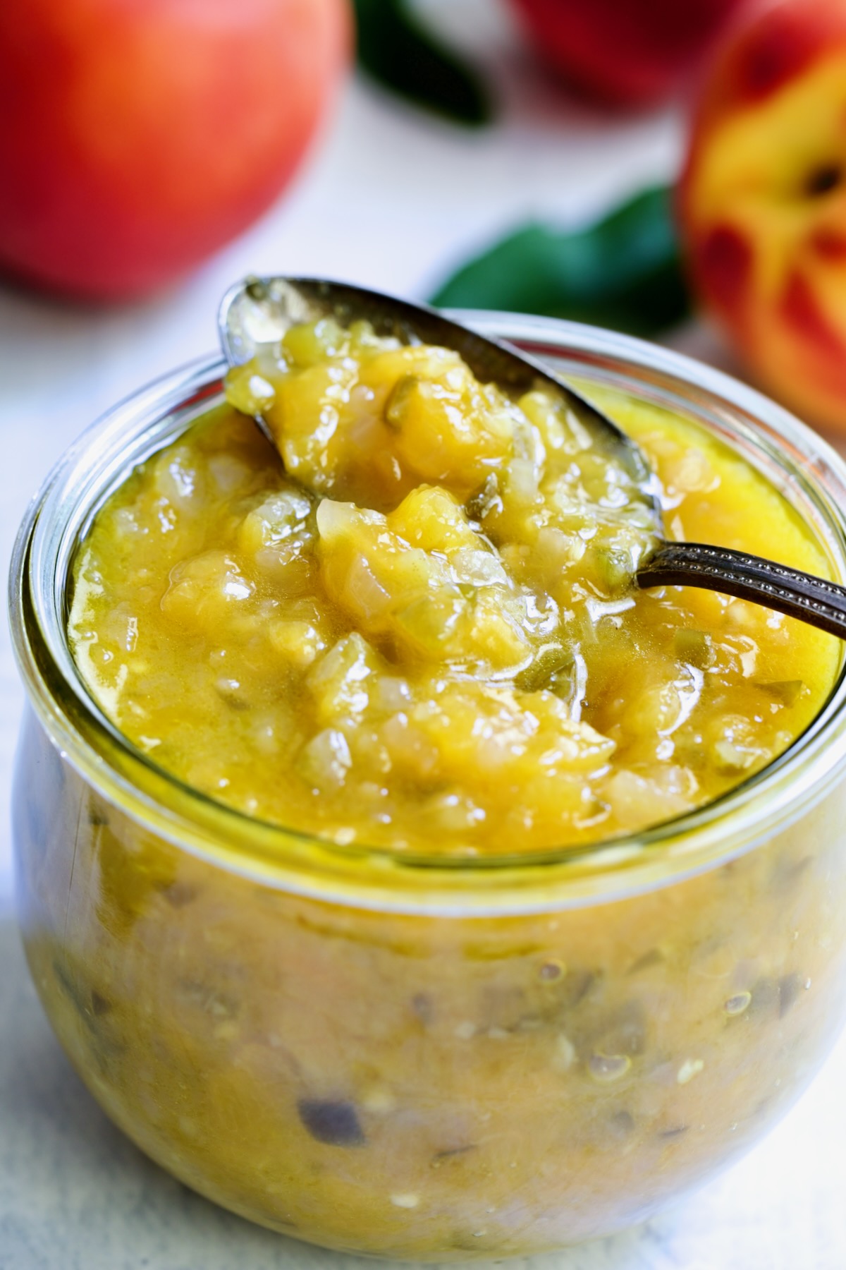 Peach Jalapeno Chutney in a glass jar with a spoon holding some.