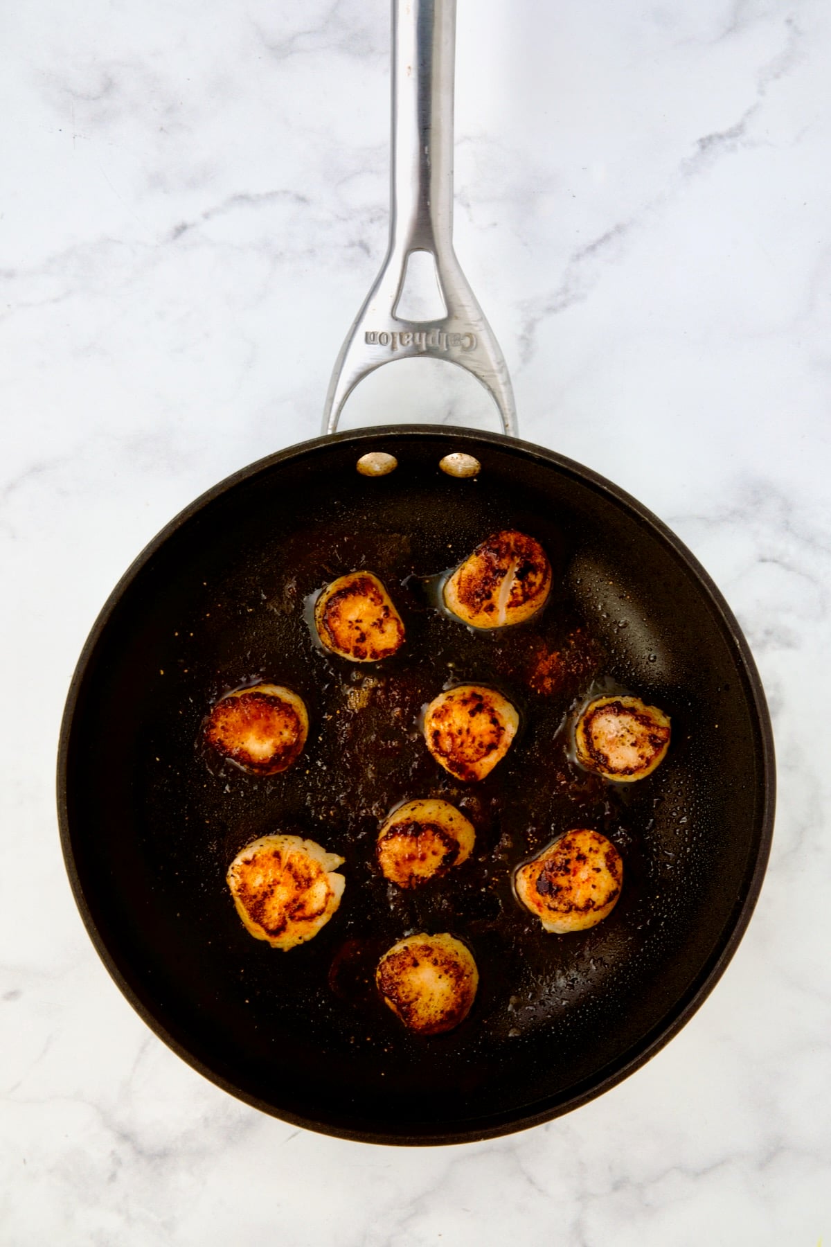 Nine seared sea scallops in nonstick skillet.