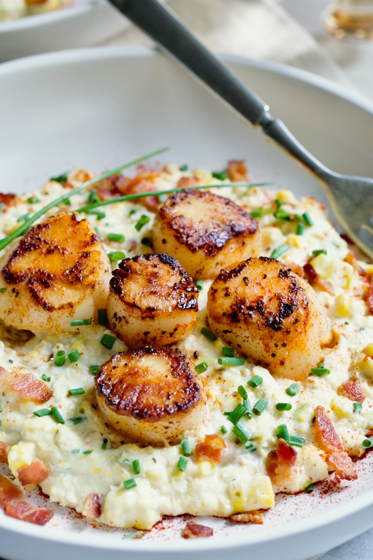 One serving of Seared Sea Scallops with Smoky Sweet Corn Puree on white plate with fork.