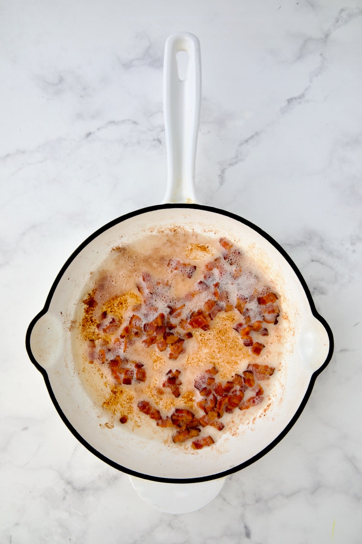Cooked crispy bacon in white enamel cast iron skillet.