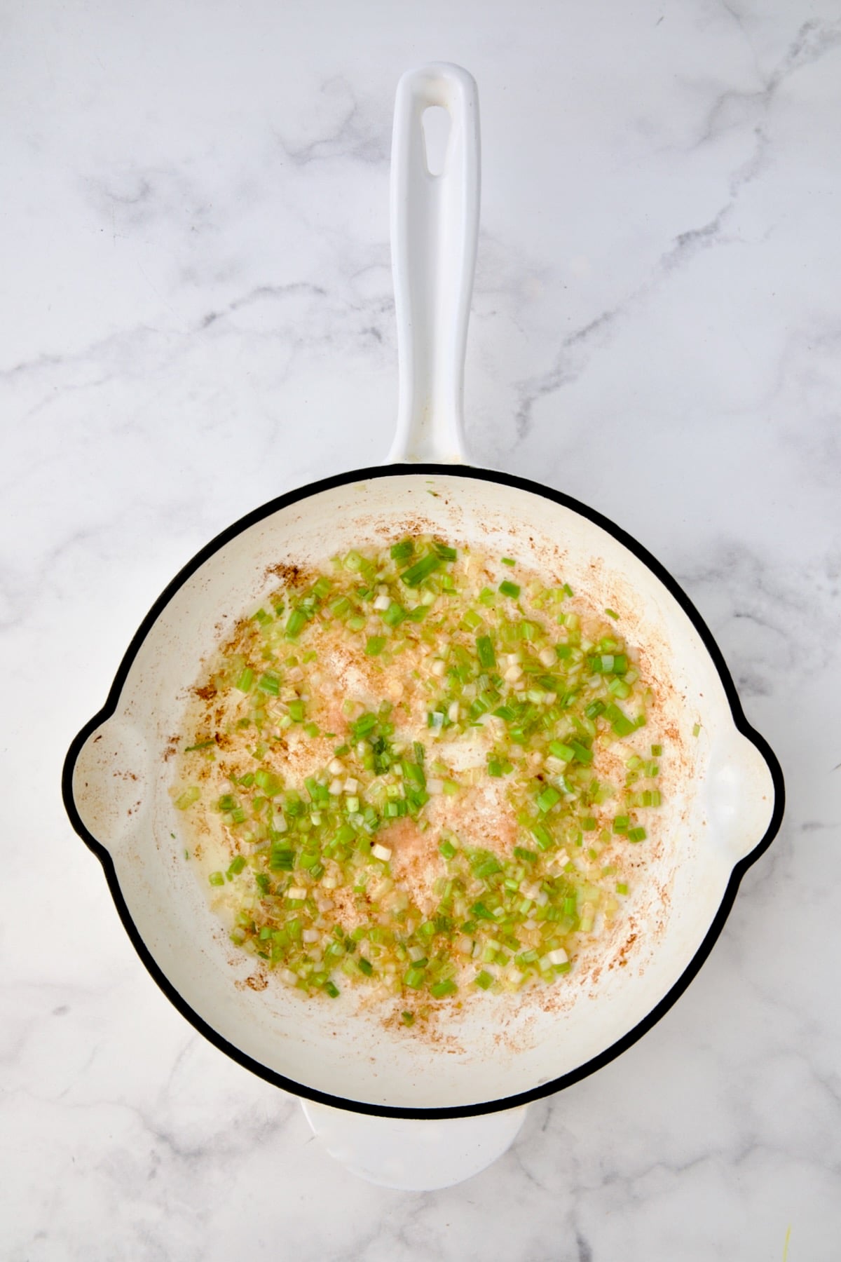 Cooked scallions in white enamel cast iron skillet.