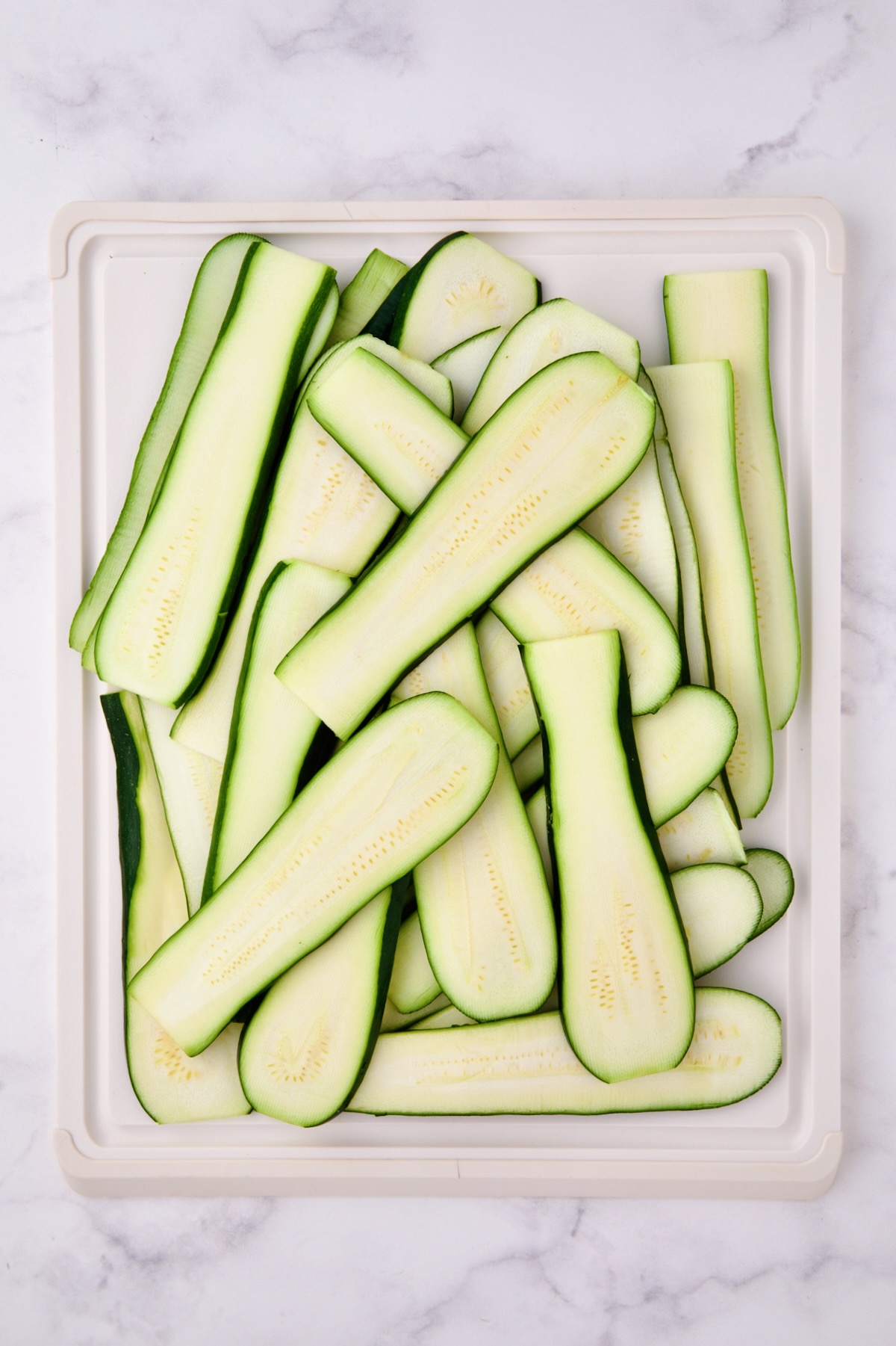 Thinly sliced zucchini on white cutting board.