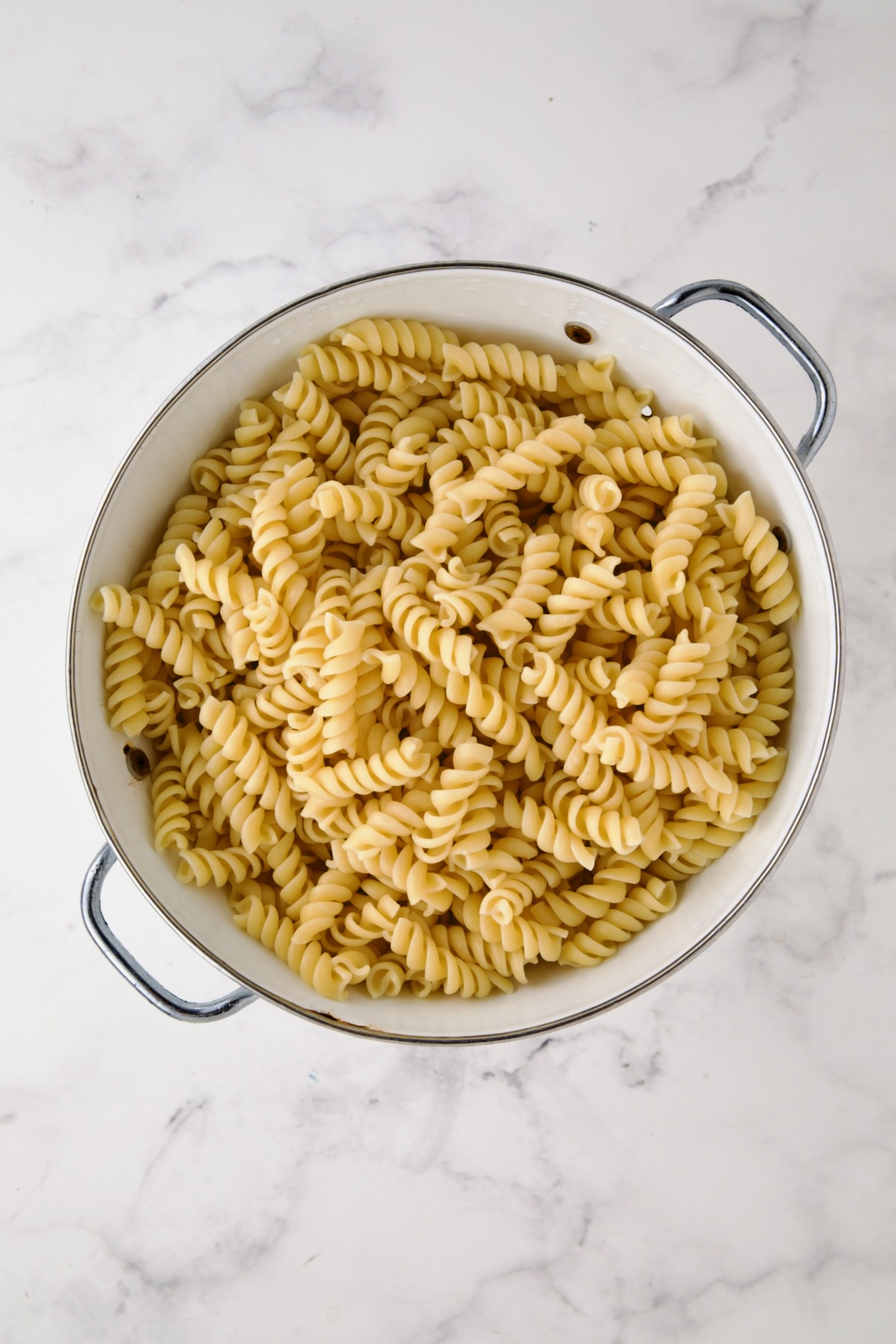Cooked rotini pasta in a white colander.