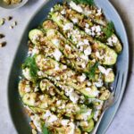 Mediterranean Grilled Zucchini with Dill Yogurt and Feta on blue platter garnished with pistachios and fresh dill sprigs.