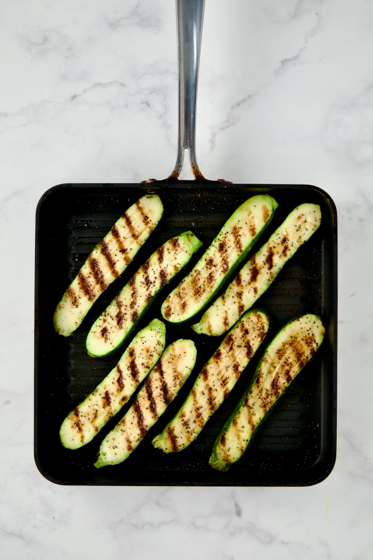 Eight grilled zucchini slices on square grill pan.
