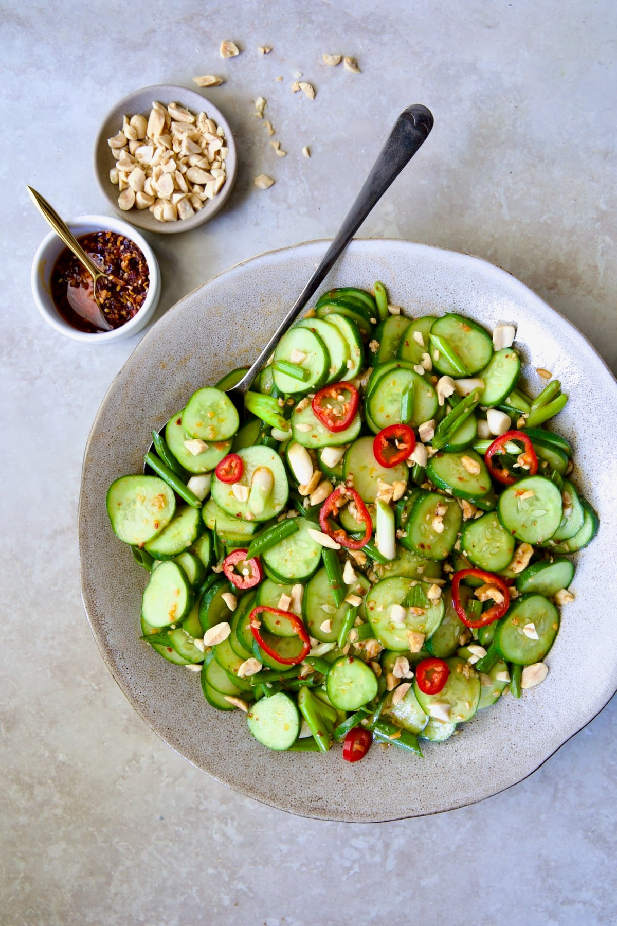 Spicy Asian Cucumber Salad in earthenware bowl with serving spoon garished with peanuts.