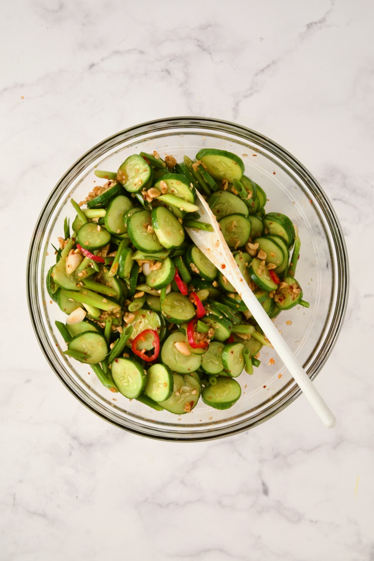 Spicy Asian Cucumber Salad being stirred together in glass bowl with white mixing spoon.