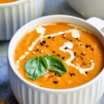 Creamy Tomato and Basil Soup in a white soup mug garnished with fresh basil leaves.