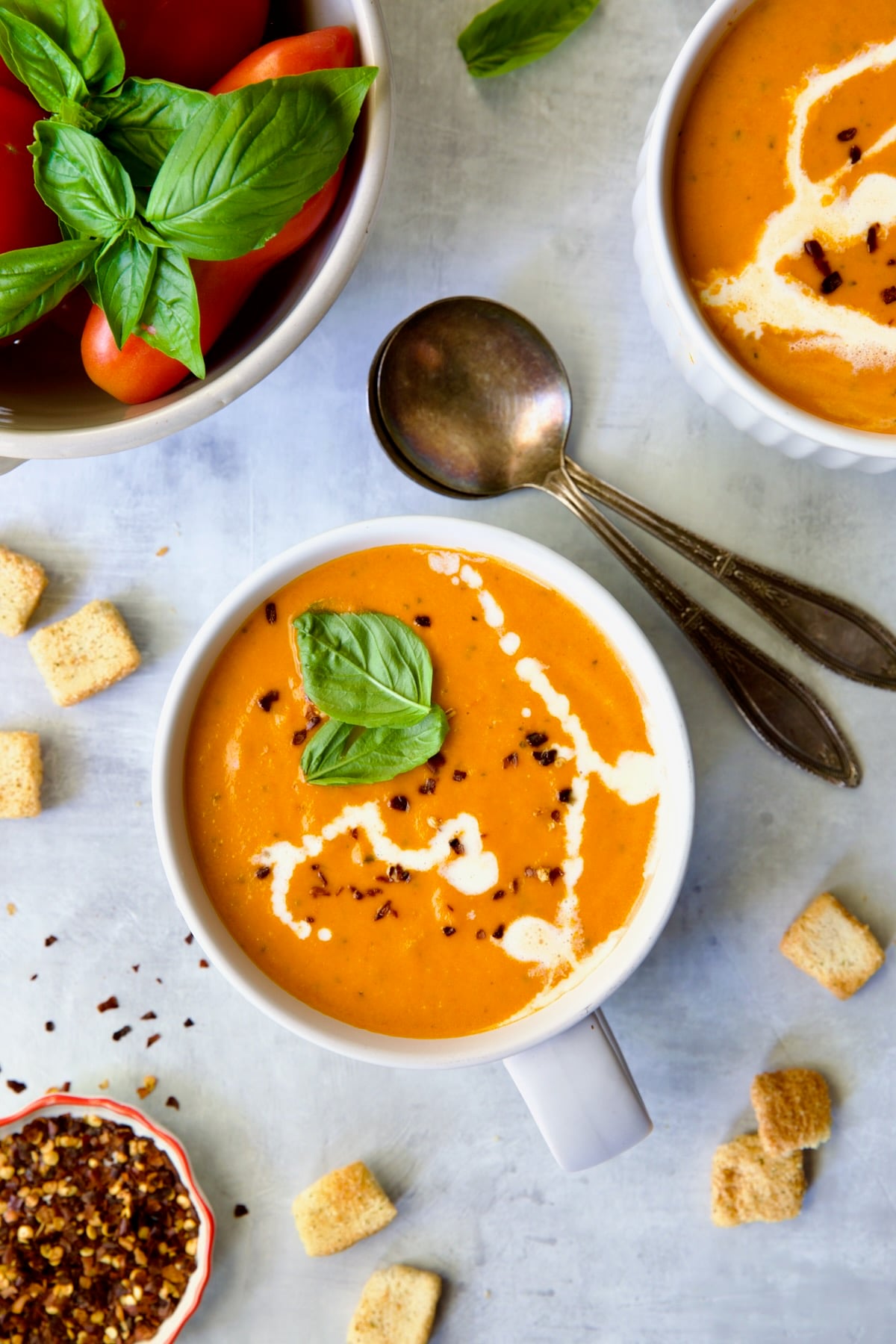 Two servings of Creamy Tomato and Basil Soup in white soup mugs garnished with fresh basil leaves.