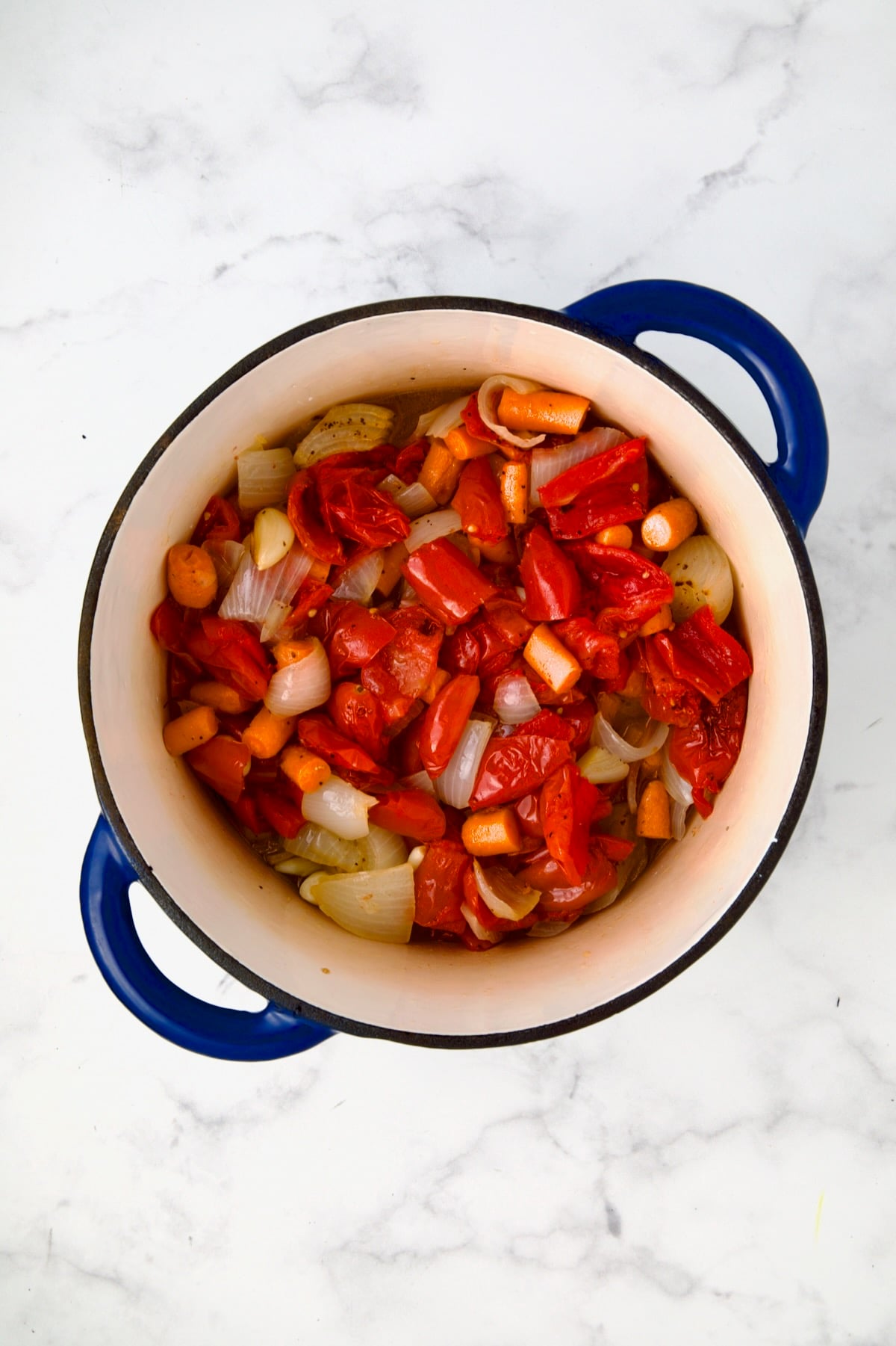 Chunks of tomatoes, onion, carrots and garlic in blue Dutch oven.