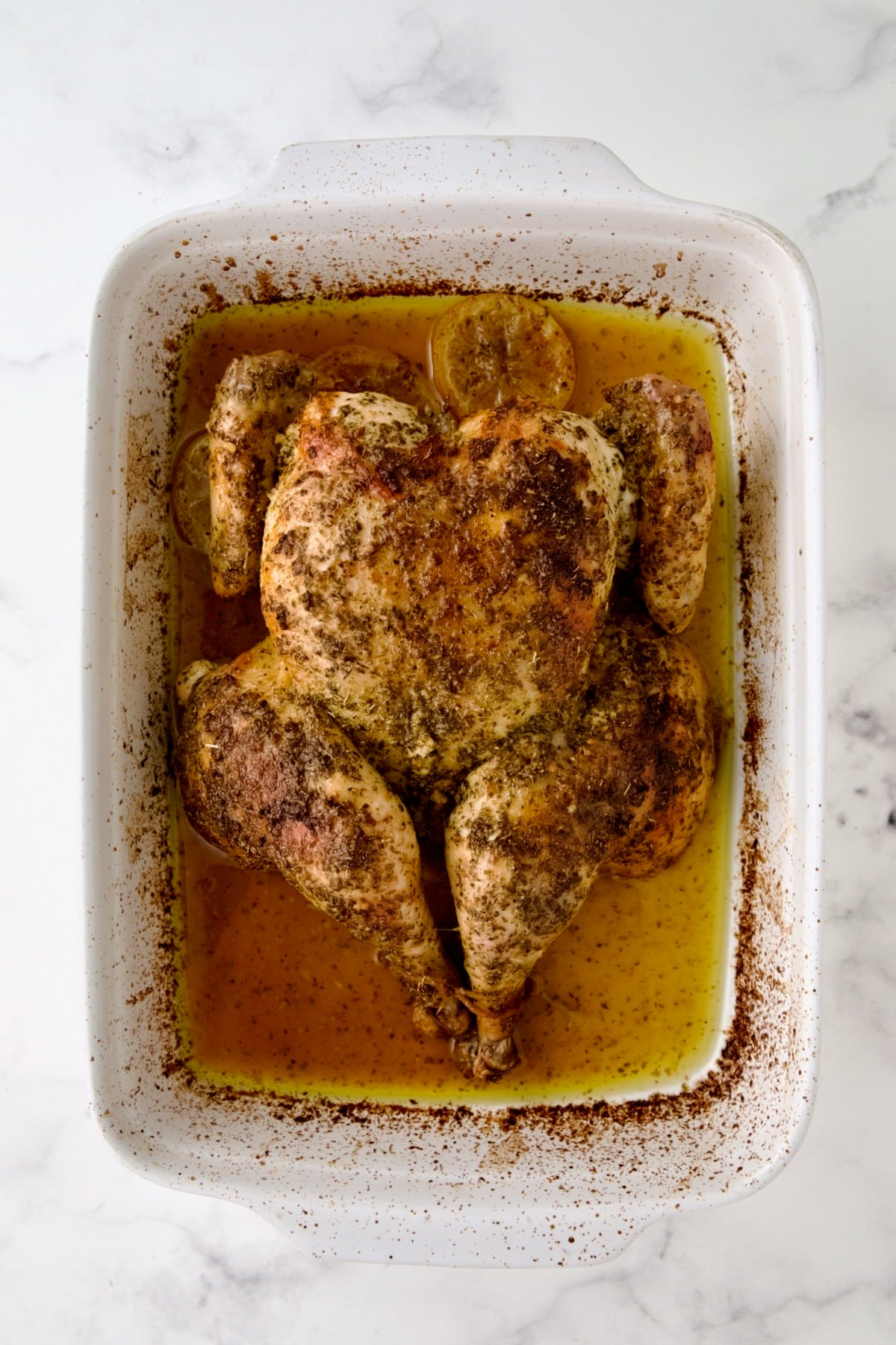 Spatchcocked fryer-size chicken after roasting in white rectangular baking dish.