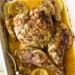 Greek Roast Chicken in white rectangular roasting pan with meat fork.