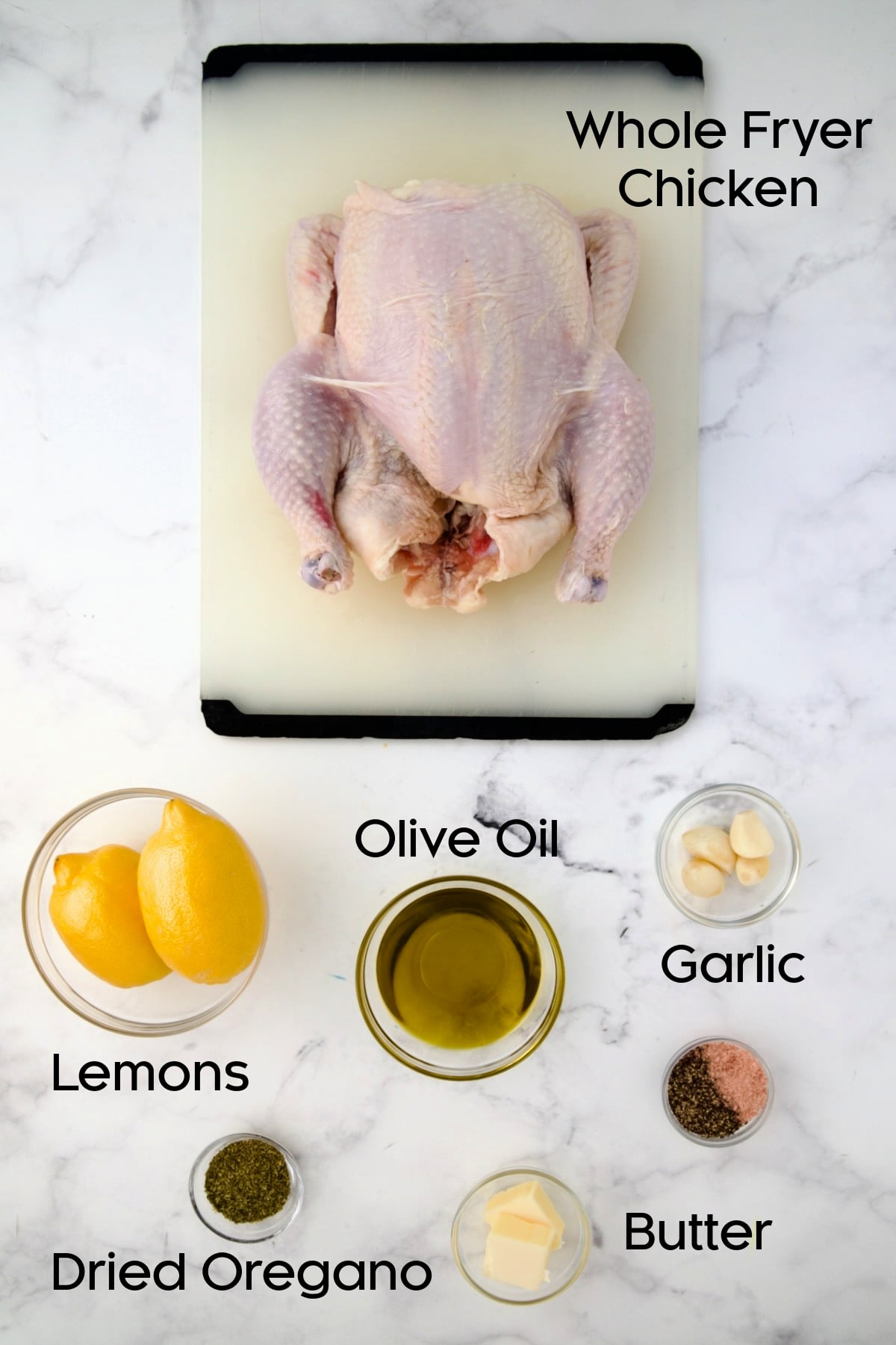 Ingredients for Greek Roast Chicken with some in glass bowls and the chicken on a white plastic cutting board.