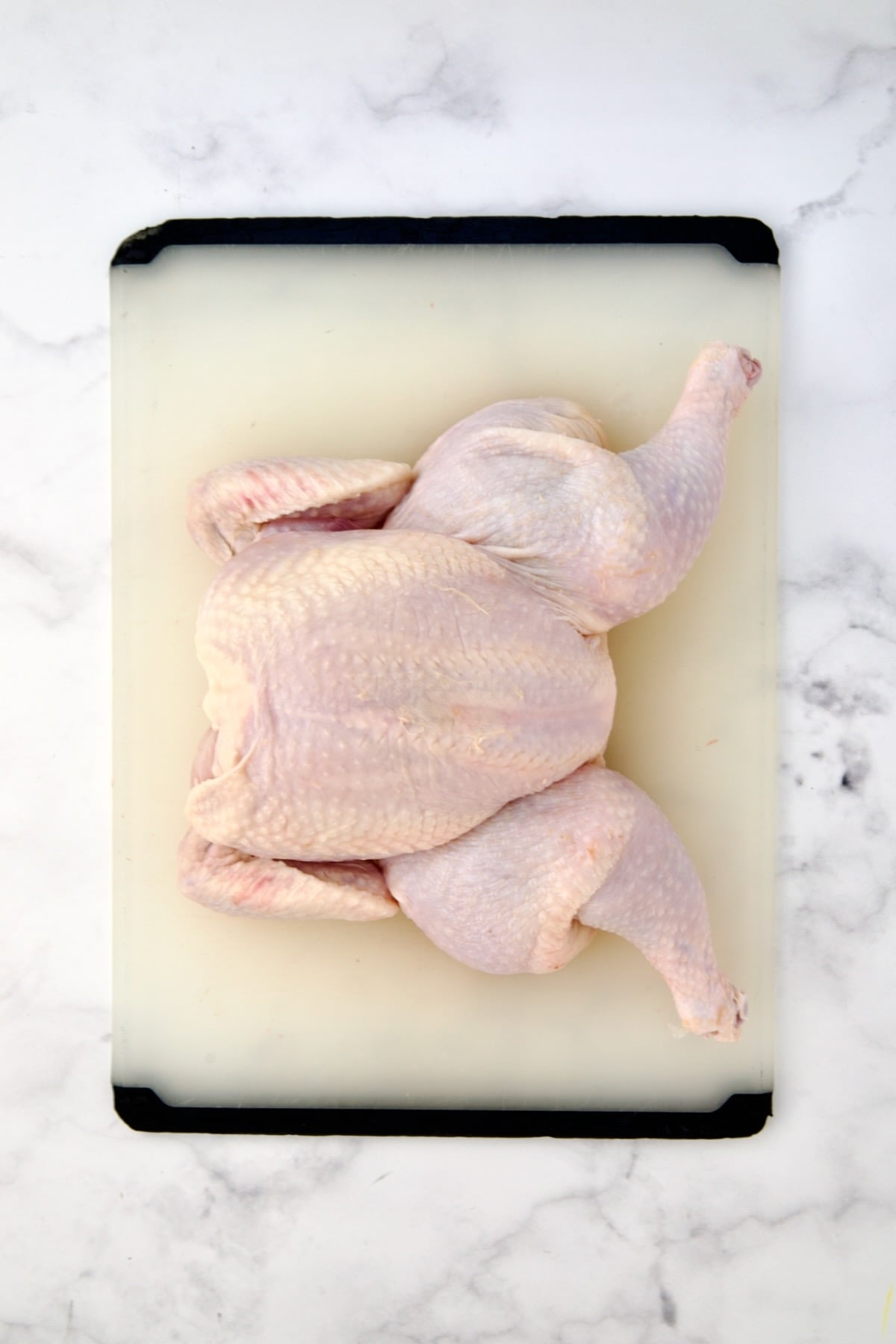 Spatchcocked fryer-size chicken on white plastic cutting board.