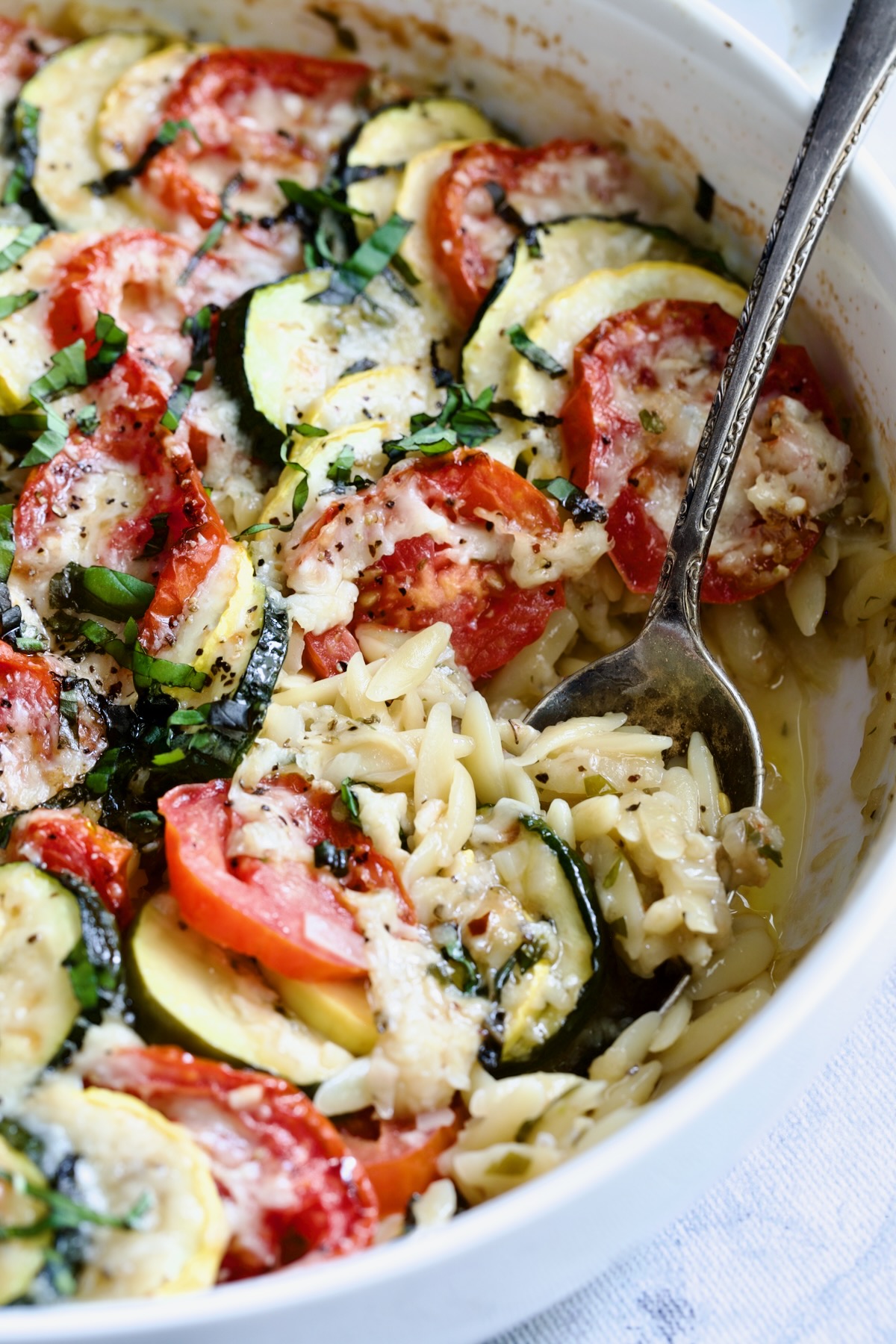 Orzo Vegetable Tian in round white baking dish with serving spoon.