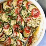 Orzo Vegetable Tian in round white baking dish with serving spoon.