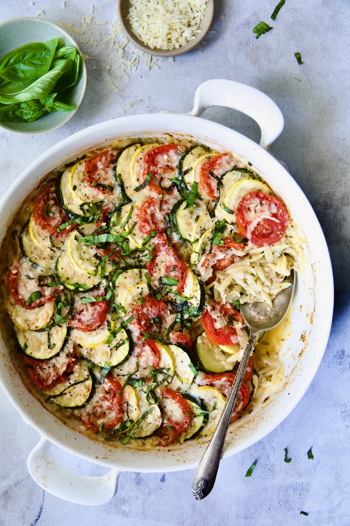 Orzo Vegetable Tian in round white baking dish with serving spoon.
