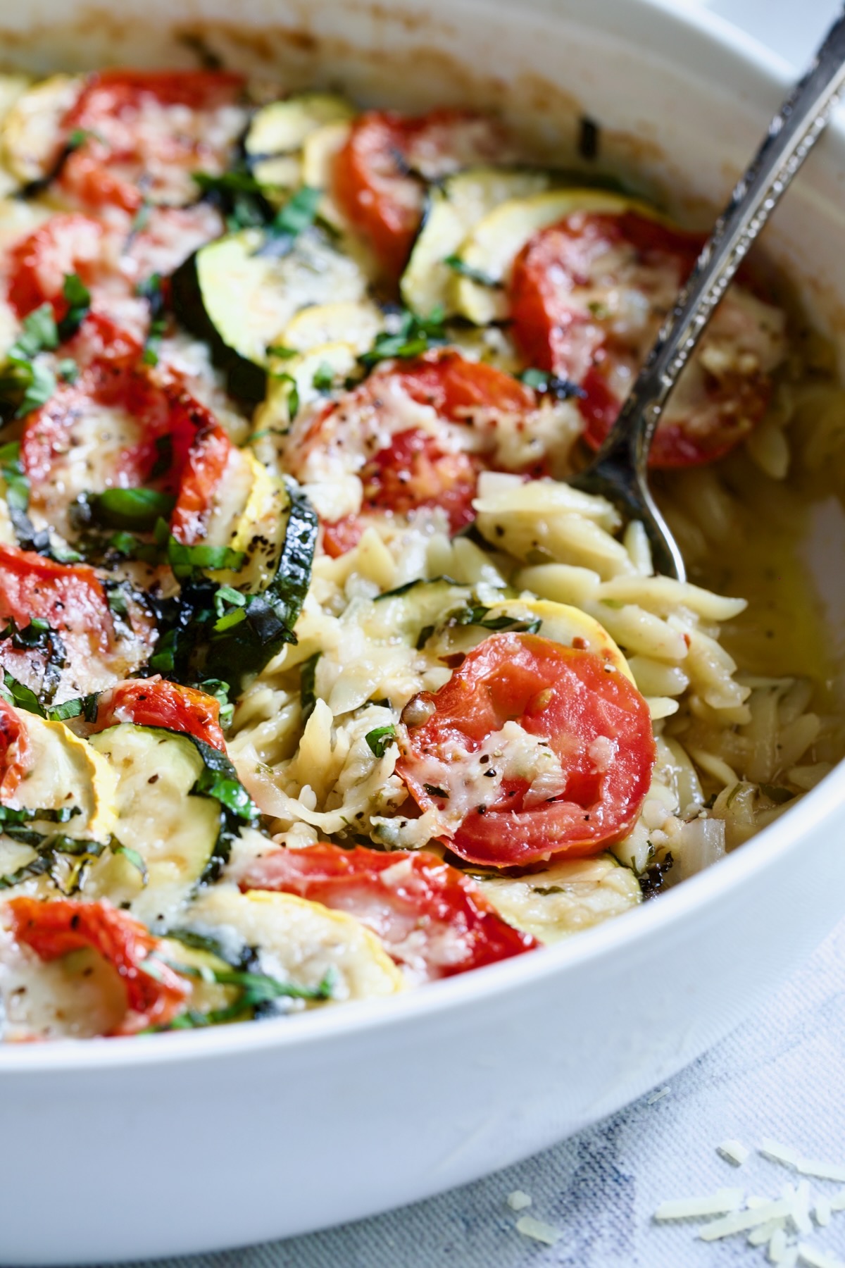 Orzo Vegetable Tian in round white baking dish with serving spoon.