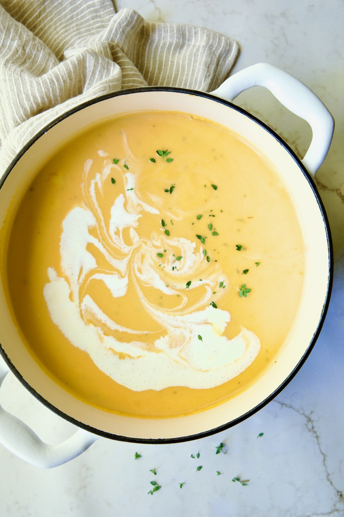 Butternut Squash Brie Soup in white enamel Dutch oven with a little extra cream and fresh thyme added for garnish.