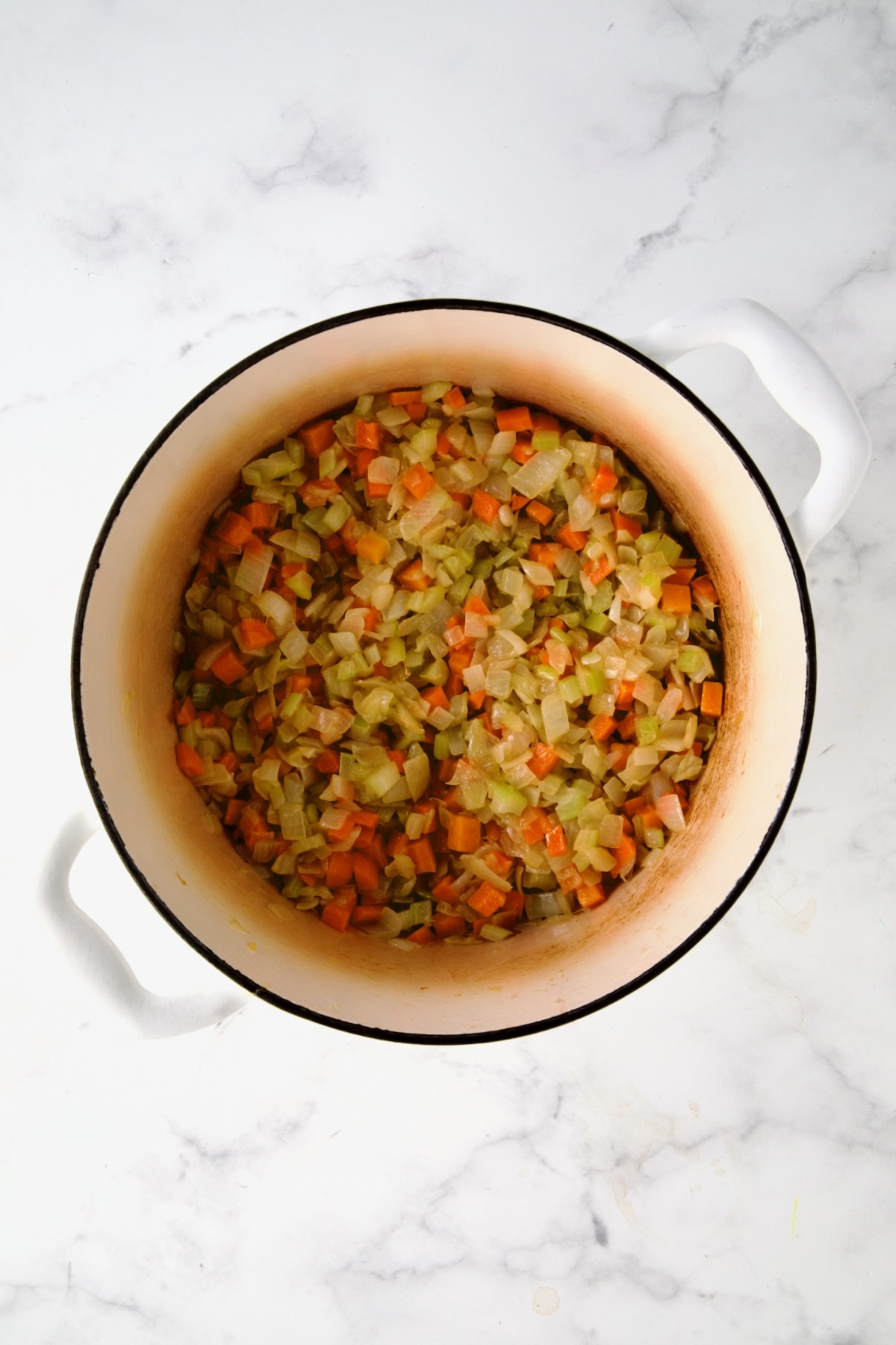 Cooked onions, celery and carrots in white enamel Dutch oven.