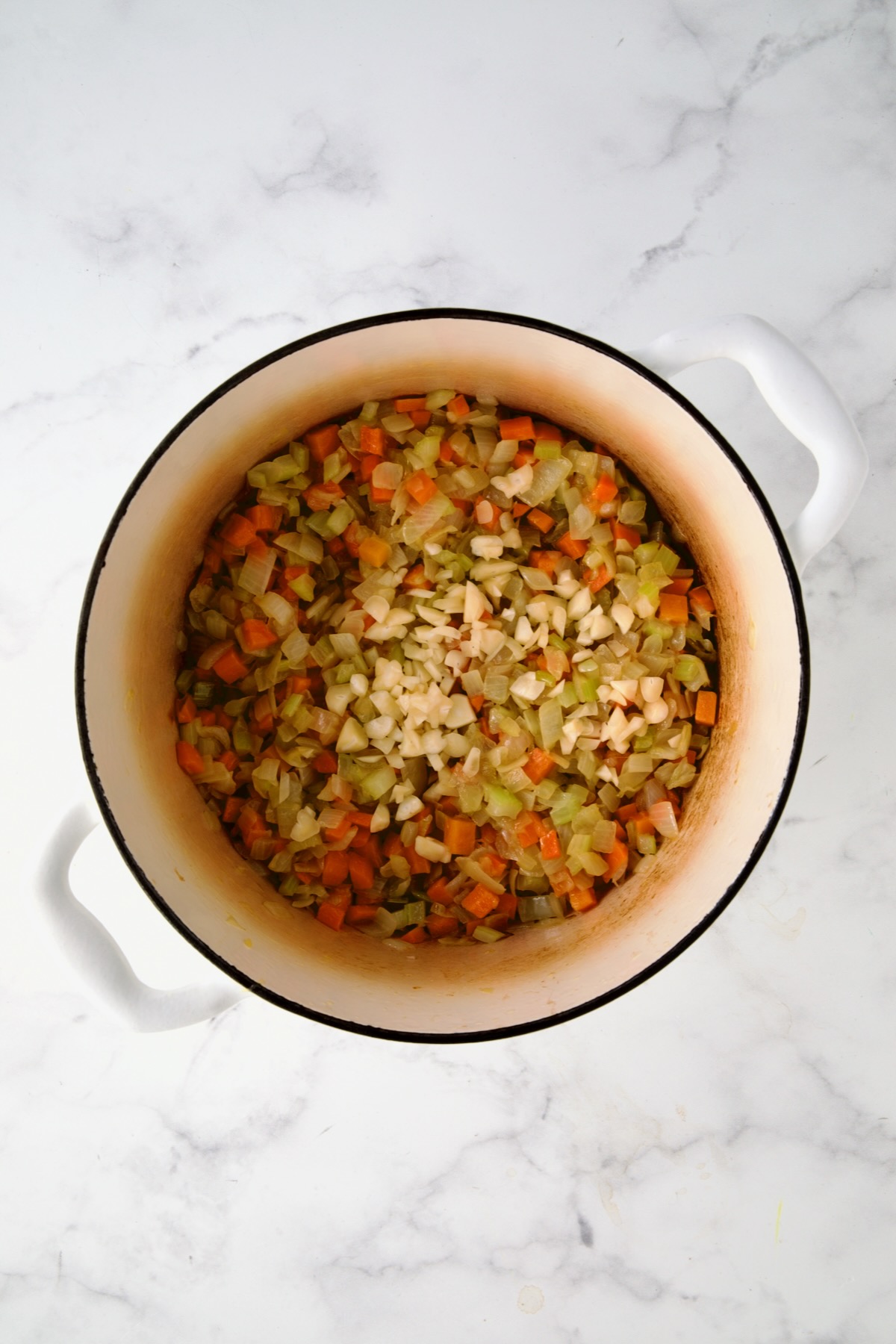 Garlic added to onions, carrots and celery in white enamel Dutch oven.